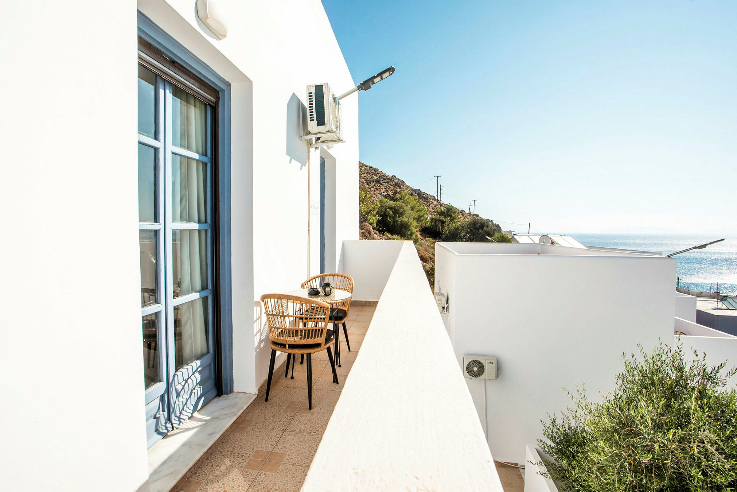 Hvid balkon med to rottingstole og et lille bord, ved siden af et hus. (AI-genereret tekst)