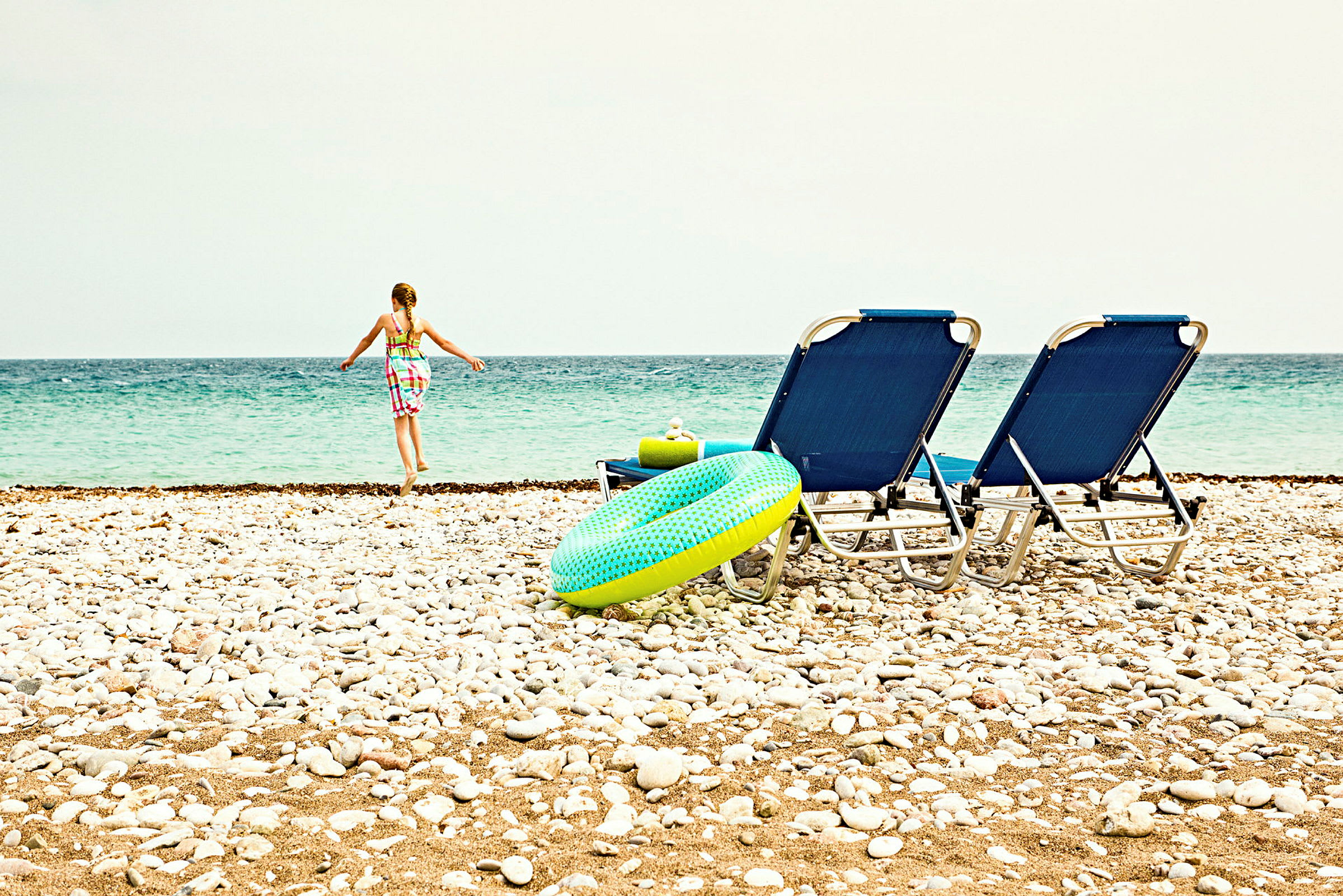 En strand med stole, en badering og en person, der går mod havet. (AI-genereret tekst)