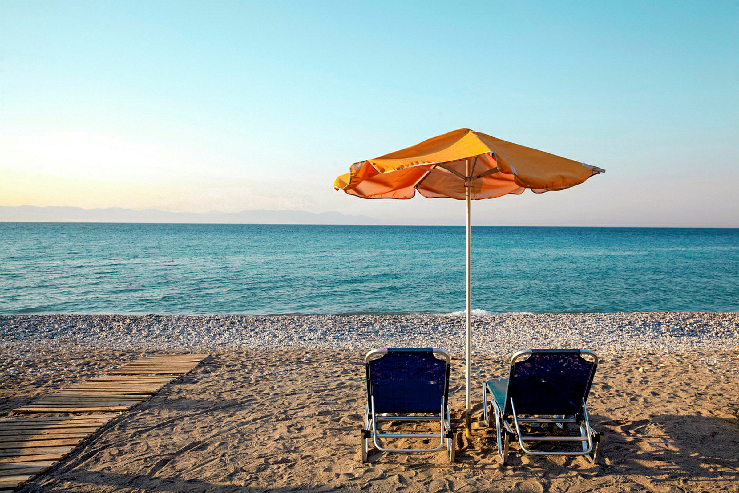 To liggestole og en parasol på en strand med udsigt over havet. (AI-genereret tekst)