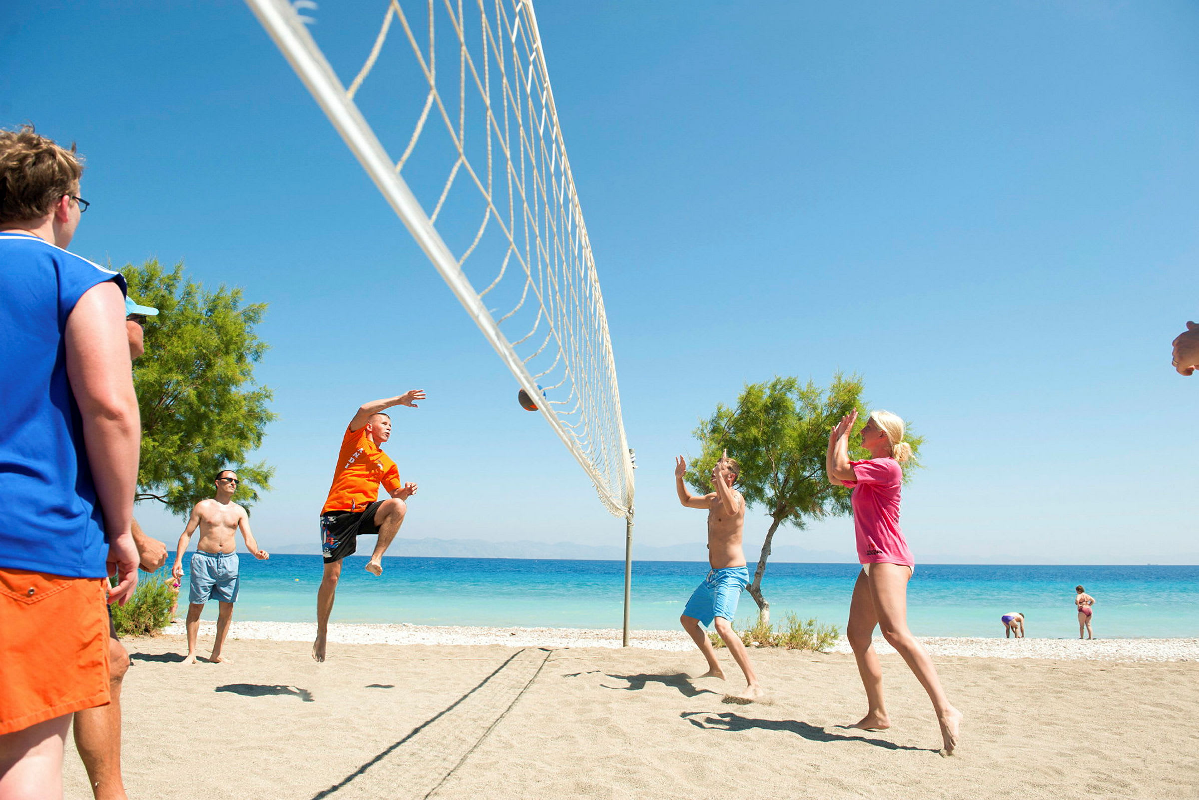 Personer spiller volleyball på en sandstrand tæt ved havet. (AI-genereret tekst)