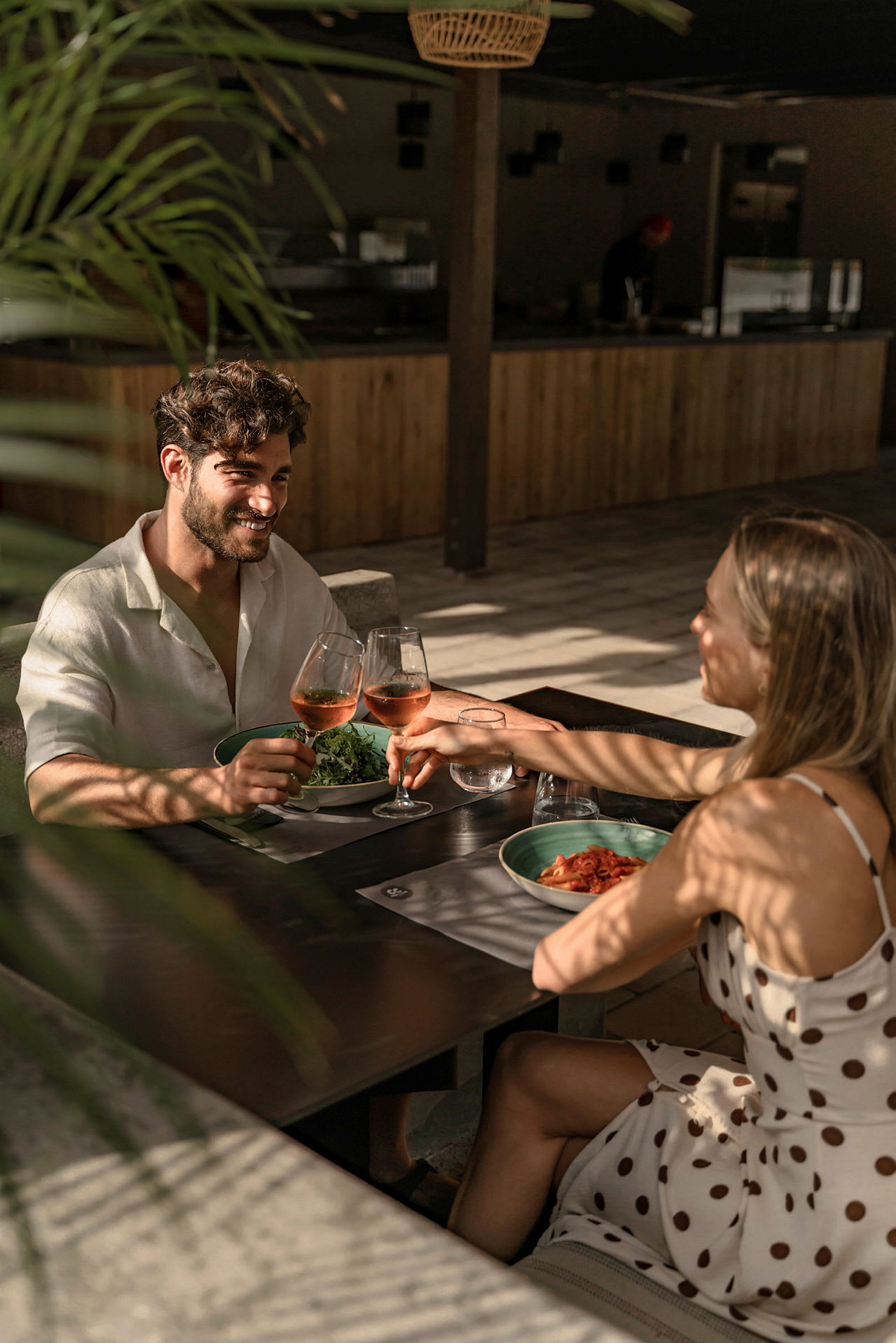 To personer skåler med glas med rosévin ved et bord på en solrig restaurant. (AI-genereret tekst)