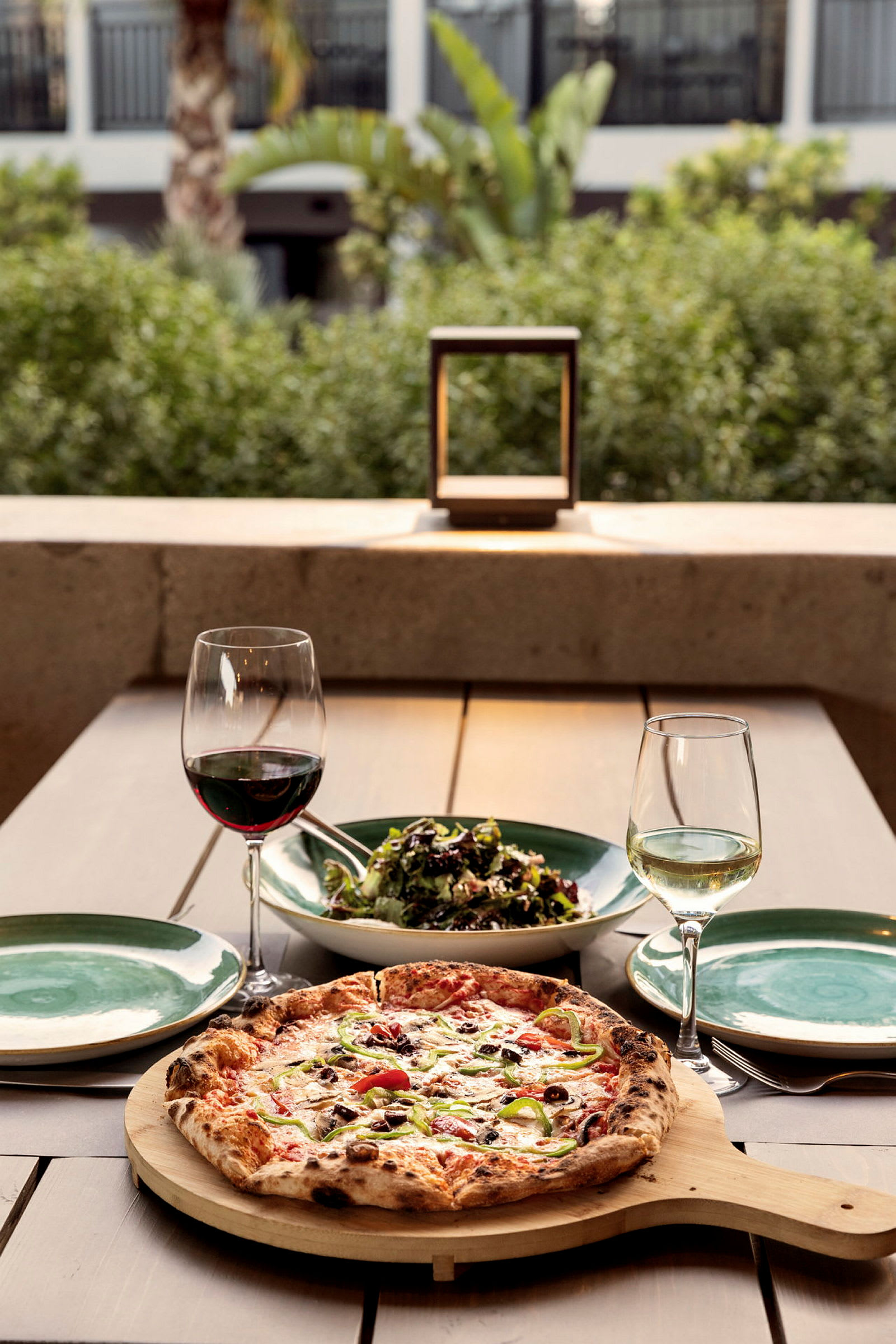 Et bord med en pizza, en skål med salat, to vinglas og tallerkener. (AI-genereret tekst)