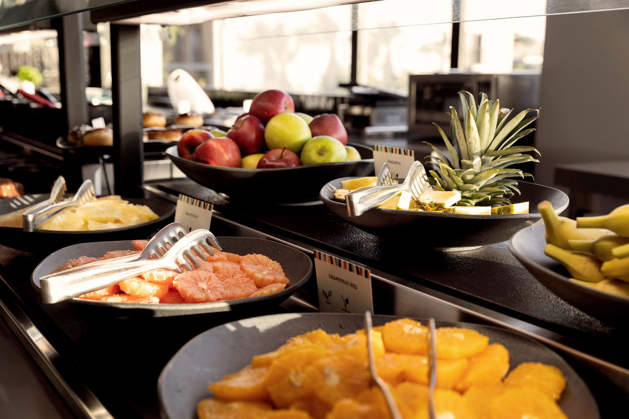 En buffet med skåle fyldt med frisk frugt, inklusive appelsiner, grapefrugter, æbler, bananer og ananas. (AI-genereret tekst)