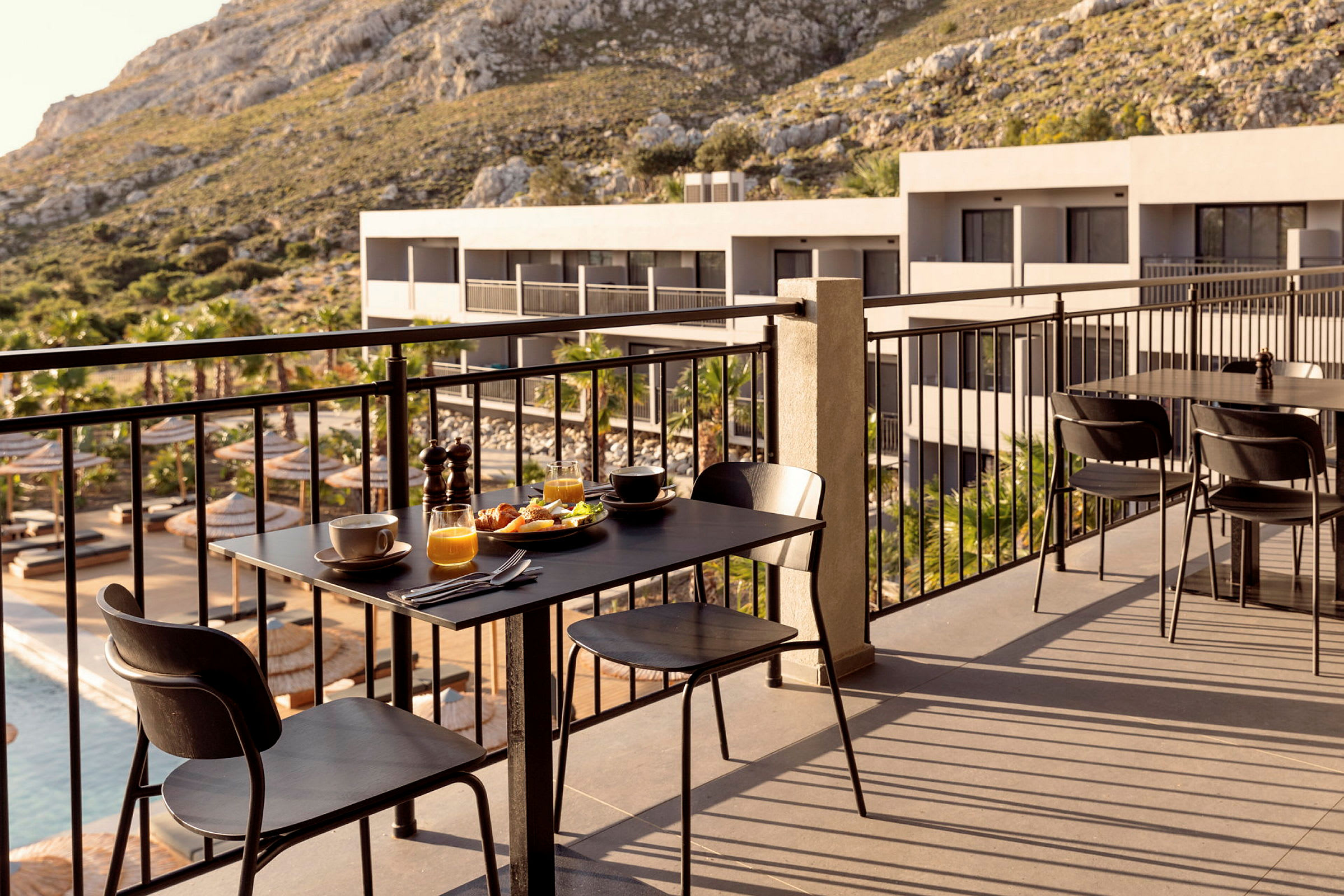 Terrasse med et dækket bord, udsigt over pool og bygninger. (AI-genereret tekst)