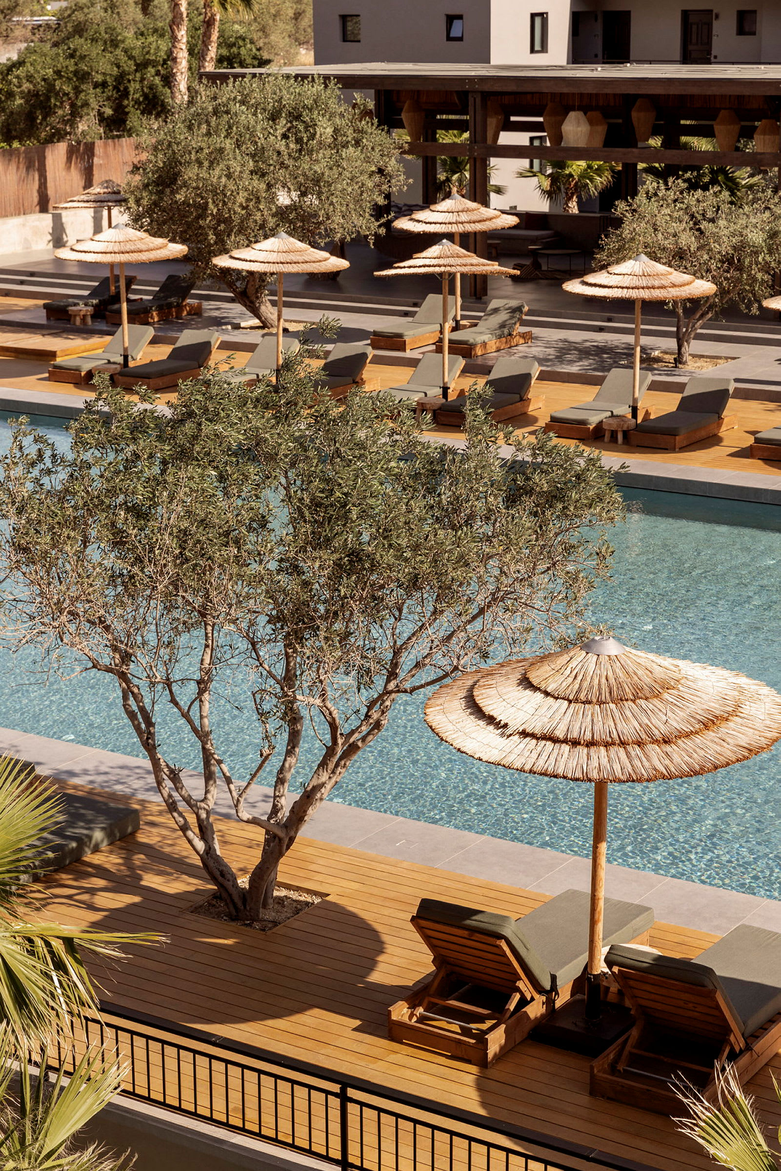 Billede af en pool med liggestole og parasoller i et hotelområde. (AI-genereret tekst)