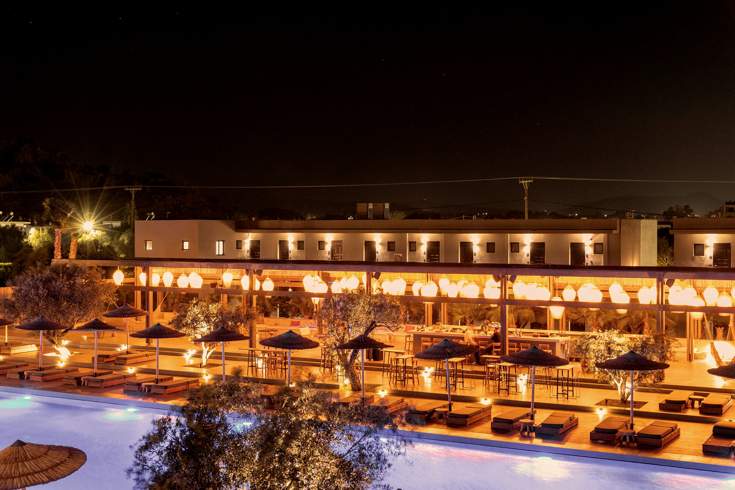 Natbillede af en oplyst hotelterrasse med siddepladser og en pool. (AI-genereret tekst)