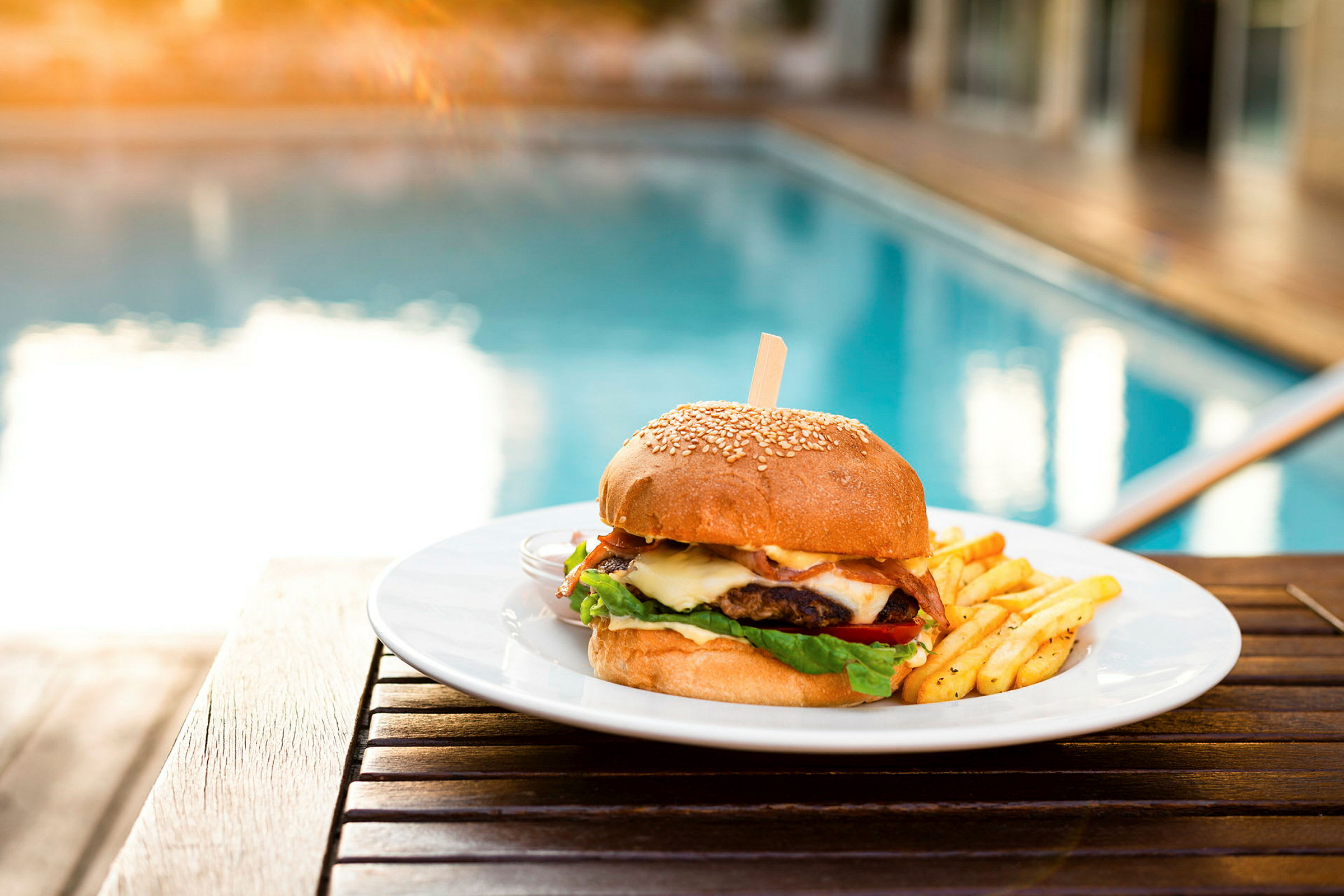 En tallerken med burger og pommes frites ved en pool. (AI-genereret tekst)