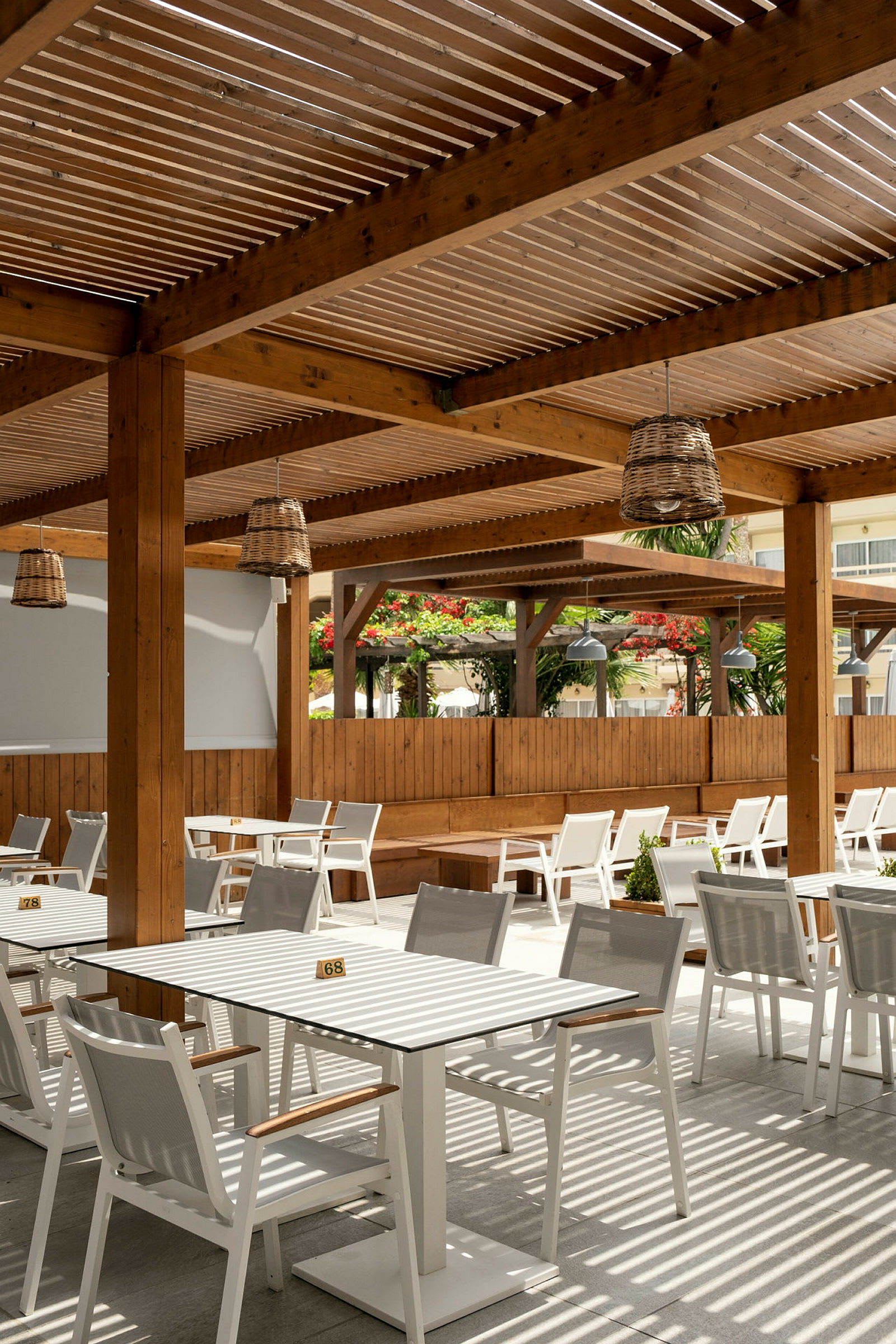 Udendørs serveringsområde med borde og stole under en træpergola. (AI-genereret tekst)