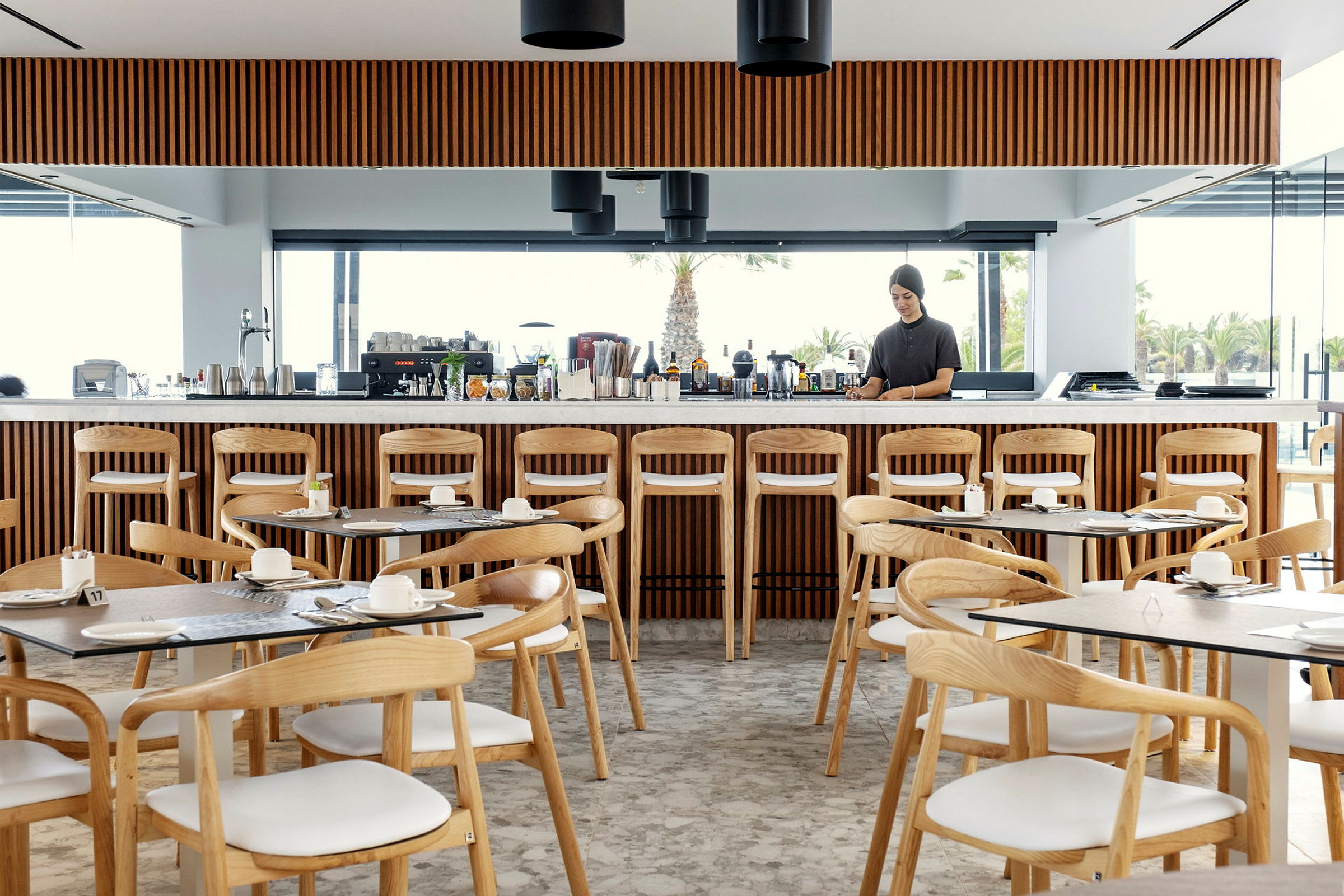 Restaurant med træstole, borde og en lang bardisk med drikkevarer. (AI-genereret tekst)