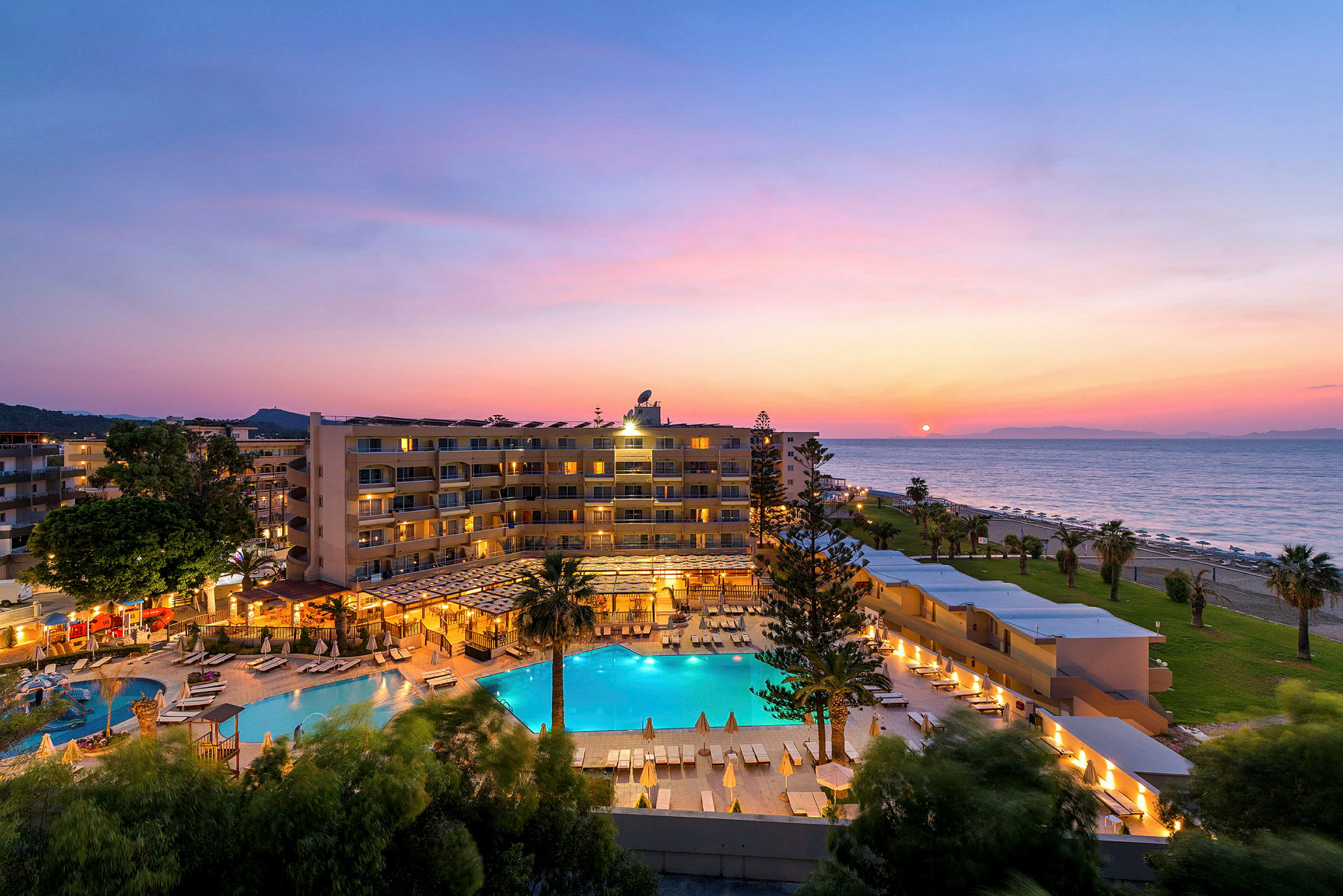 Hotelområde med pool, tæt på stranden ved solnedgang. (AI-genereret tekst)