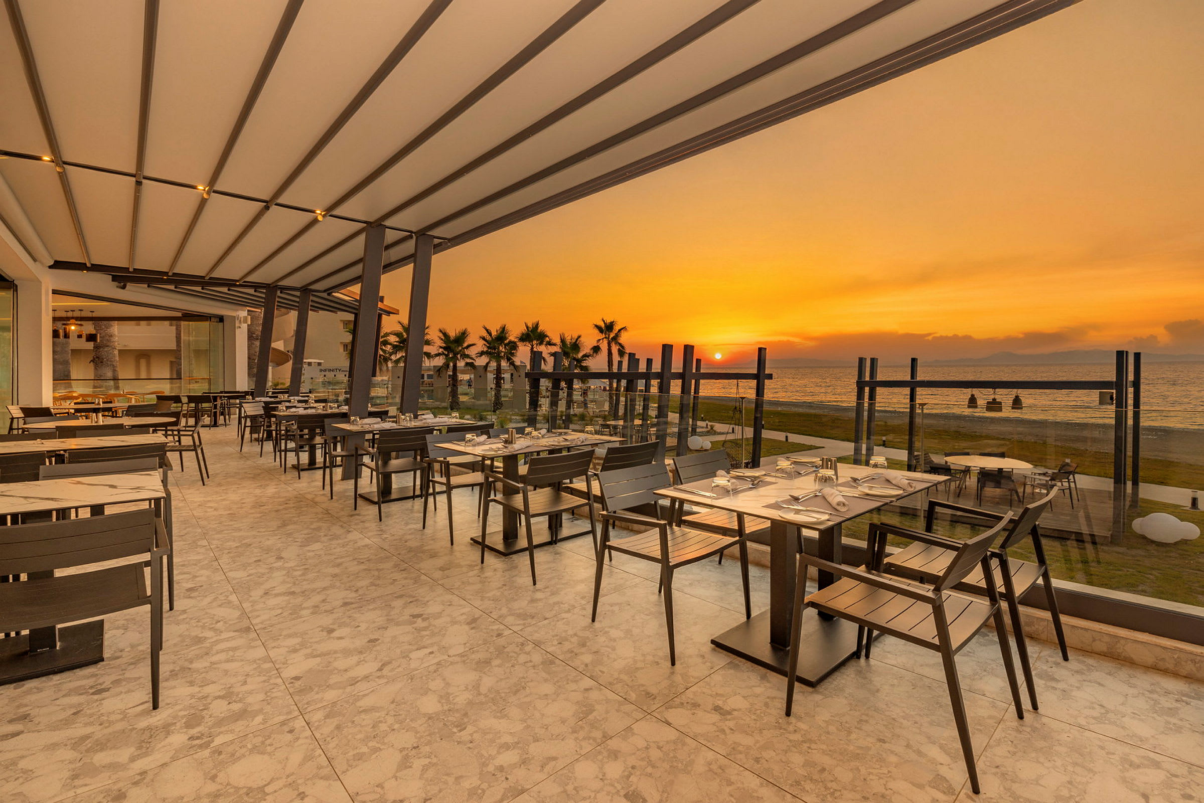 En udendørs restaurant med udsigt over havet ved solnedgang. (AI-genereret tekst)
