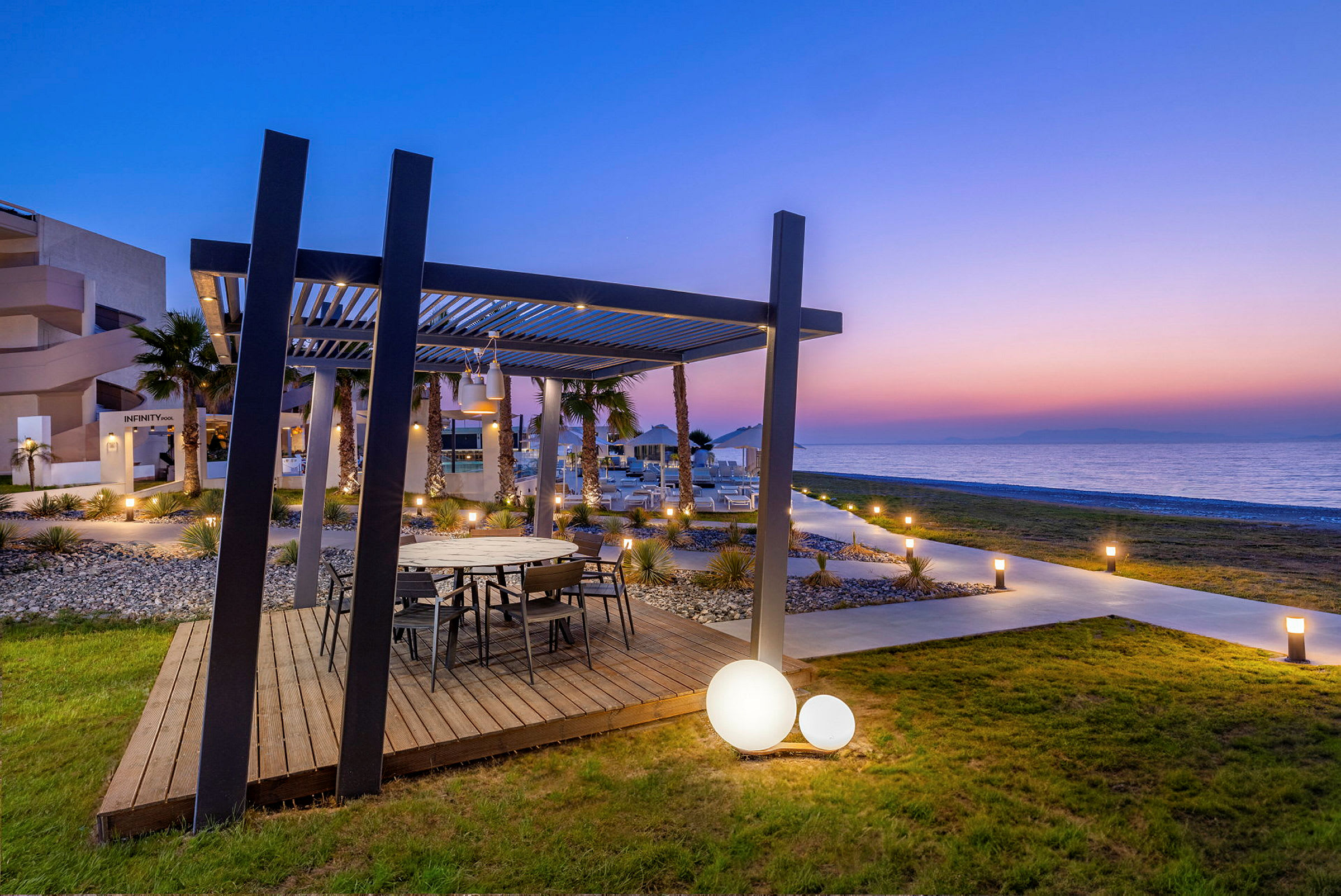 Et udendørs område med et træbord under en pergola, med havudsigt i solnedgang. (AI-genereret tekst)
