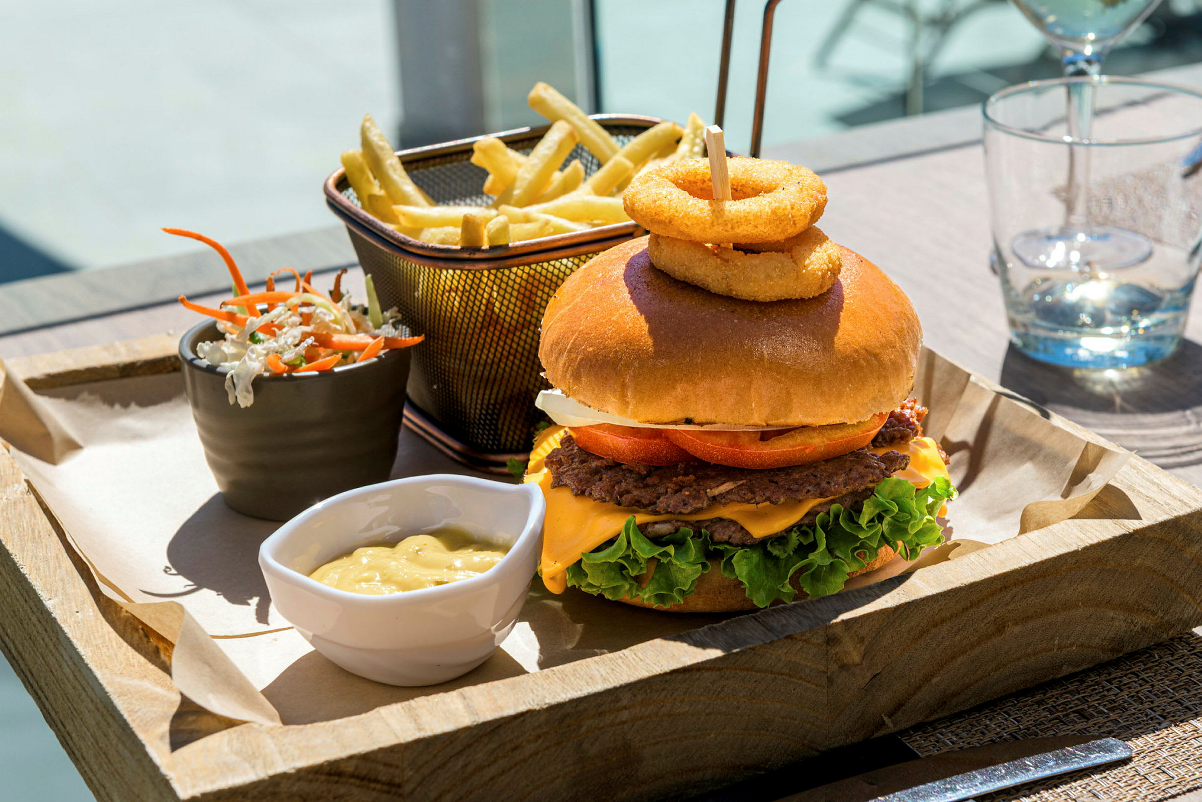 Et måltid med burger, pommes frites, salatblanding og sovs serveres på en træbakke. (AI-genereret tekst)