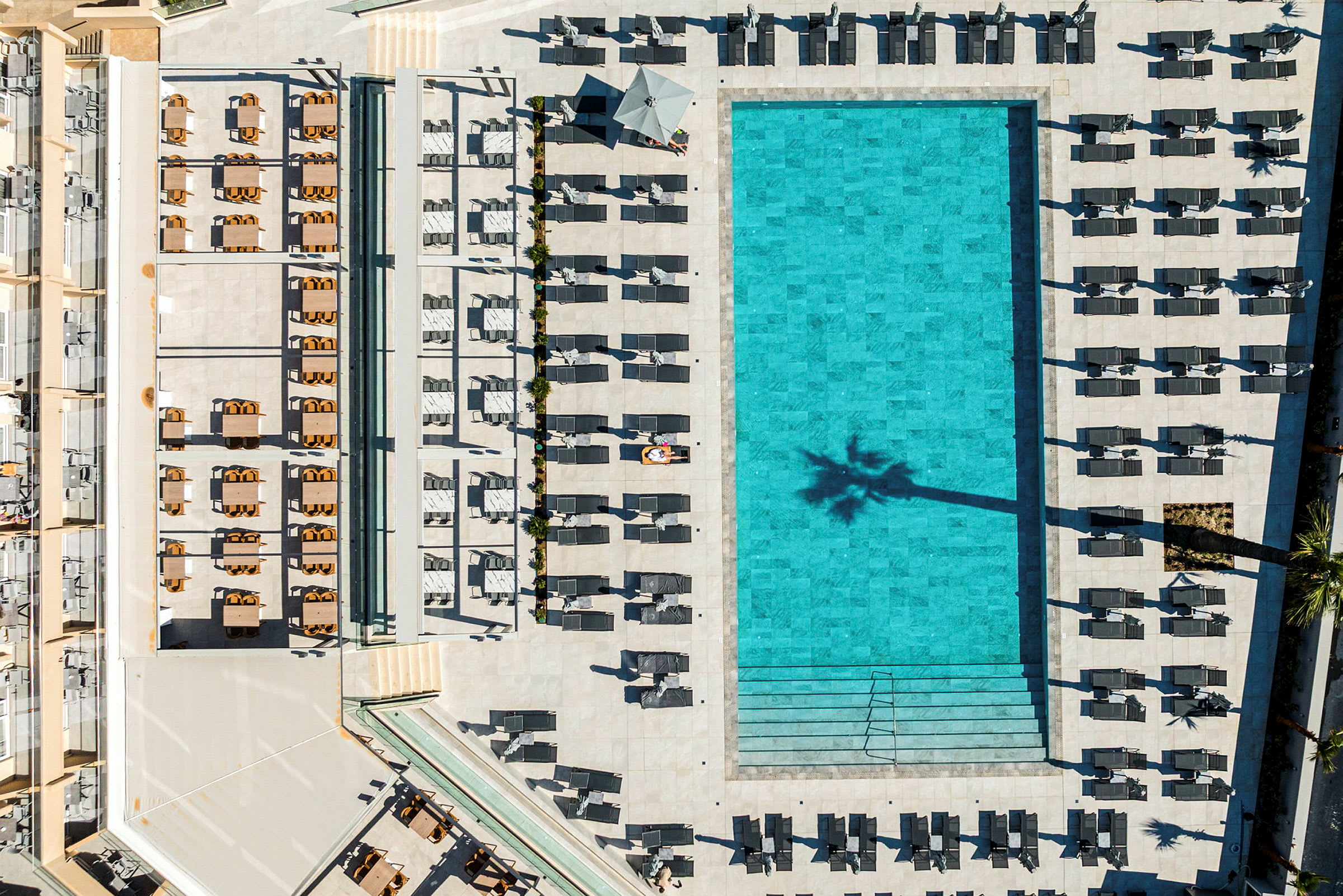 Luftfoto af en stor, rektangulær pool omgivet af liggestole og parasoller. (AI-genereret tekst)