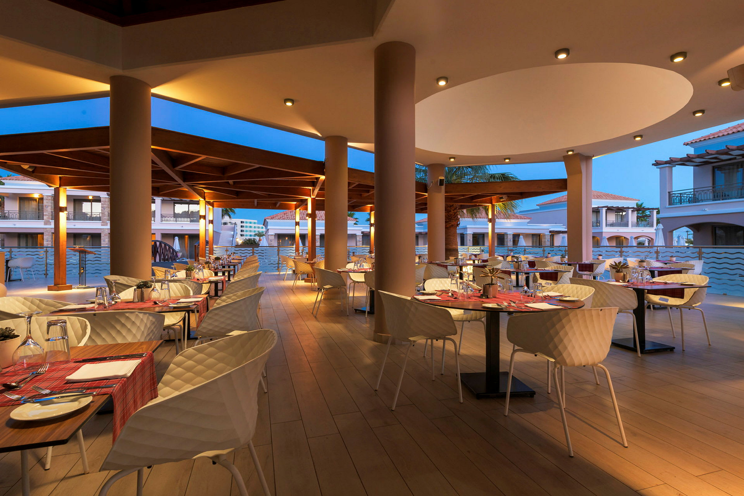 Spiseområde med borde og stole udendørs på en restaurant med aftenbelysning. (AI-genereret tekst)