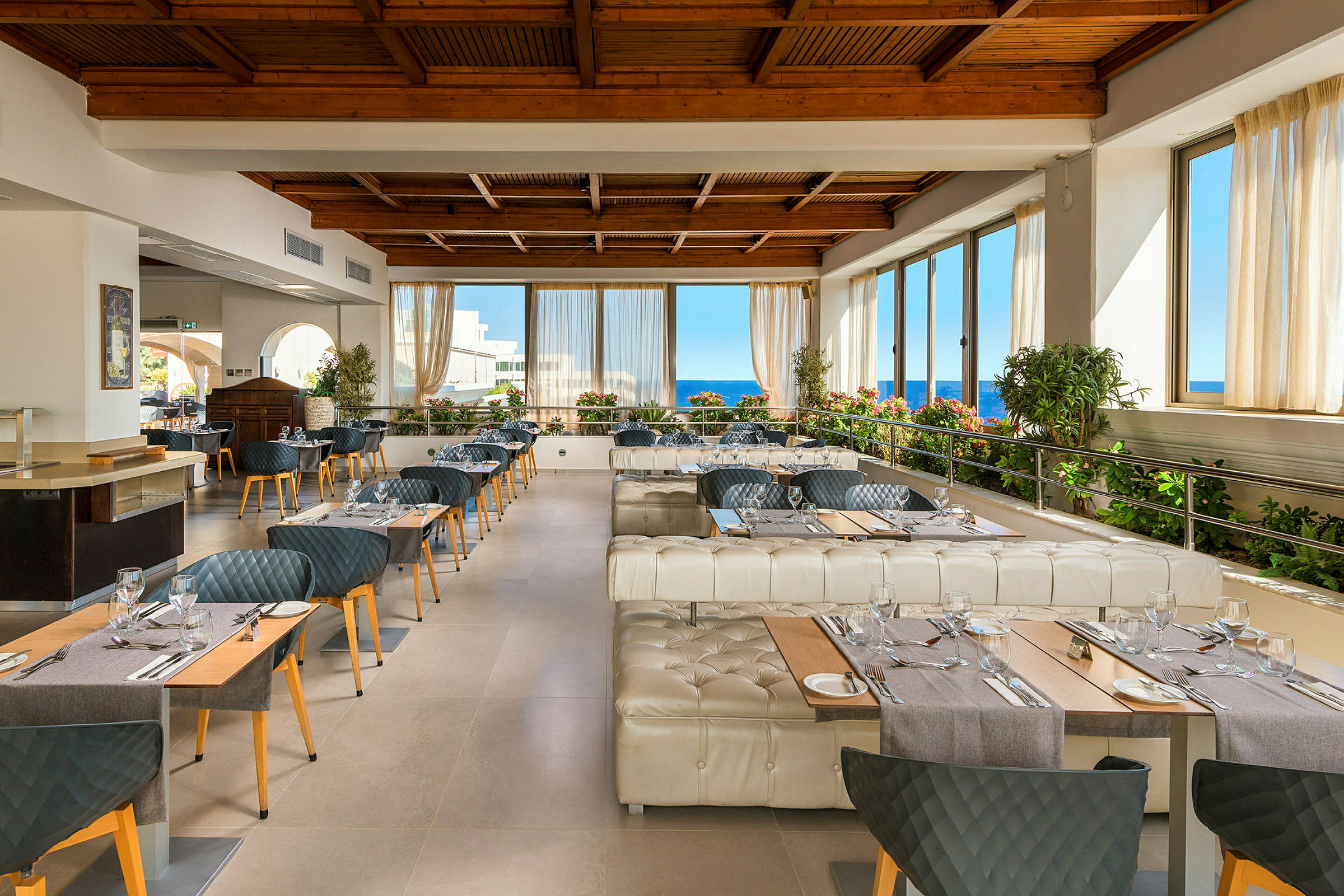 Restaurant med borde, stole og vinduer med udsigt til havet. (AI-genereret tekst)