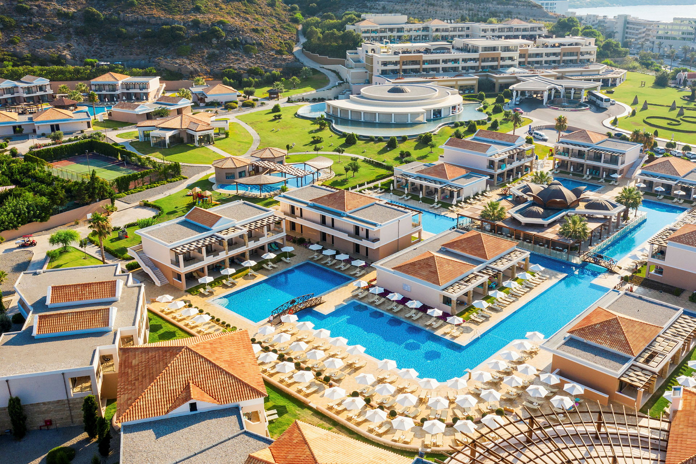 Luftfoto af en resort med pools, bygninger og grønne områder. (AI-genereret tekst)
