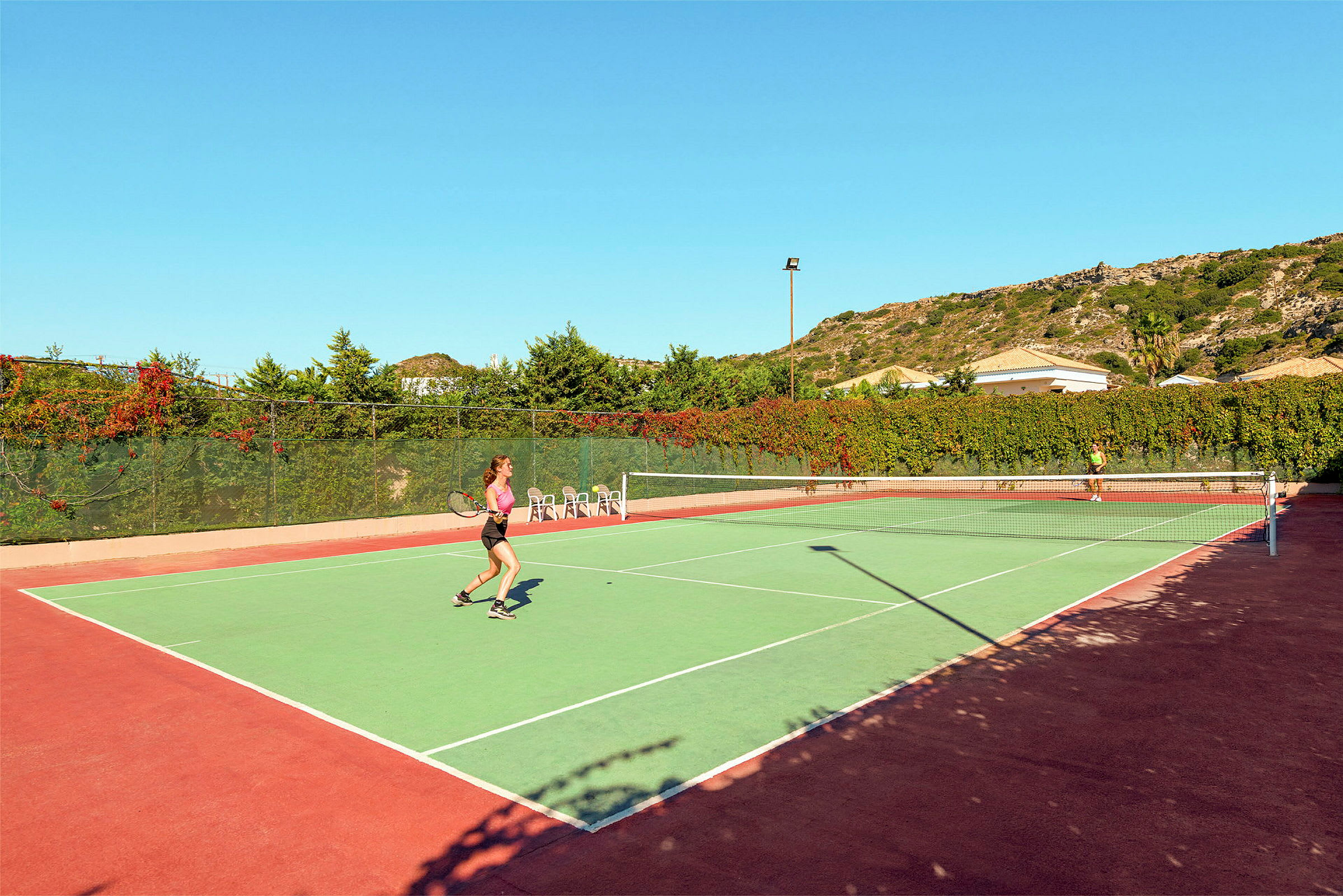 To personer spiller tennis på en udendørsbane under klar himmel. (AI-genereret tekst)