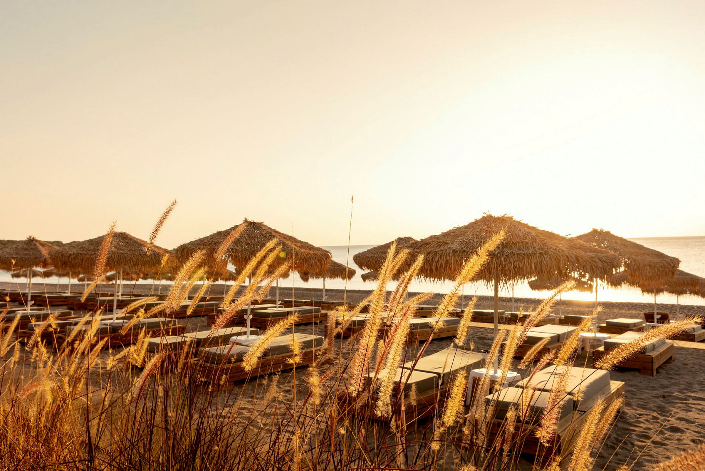 Billede af liggestole og parasoller på en sandstrand under solnedgang. (AI-genereret tekst)