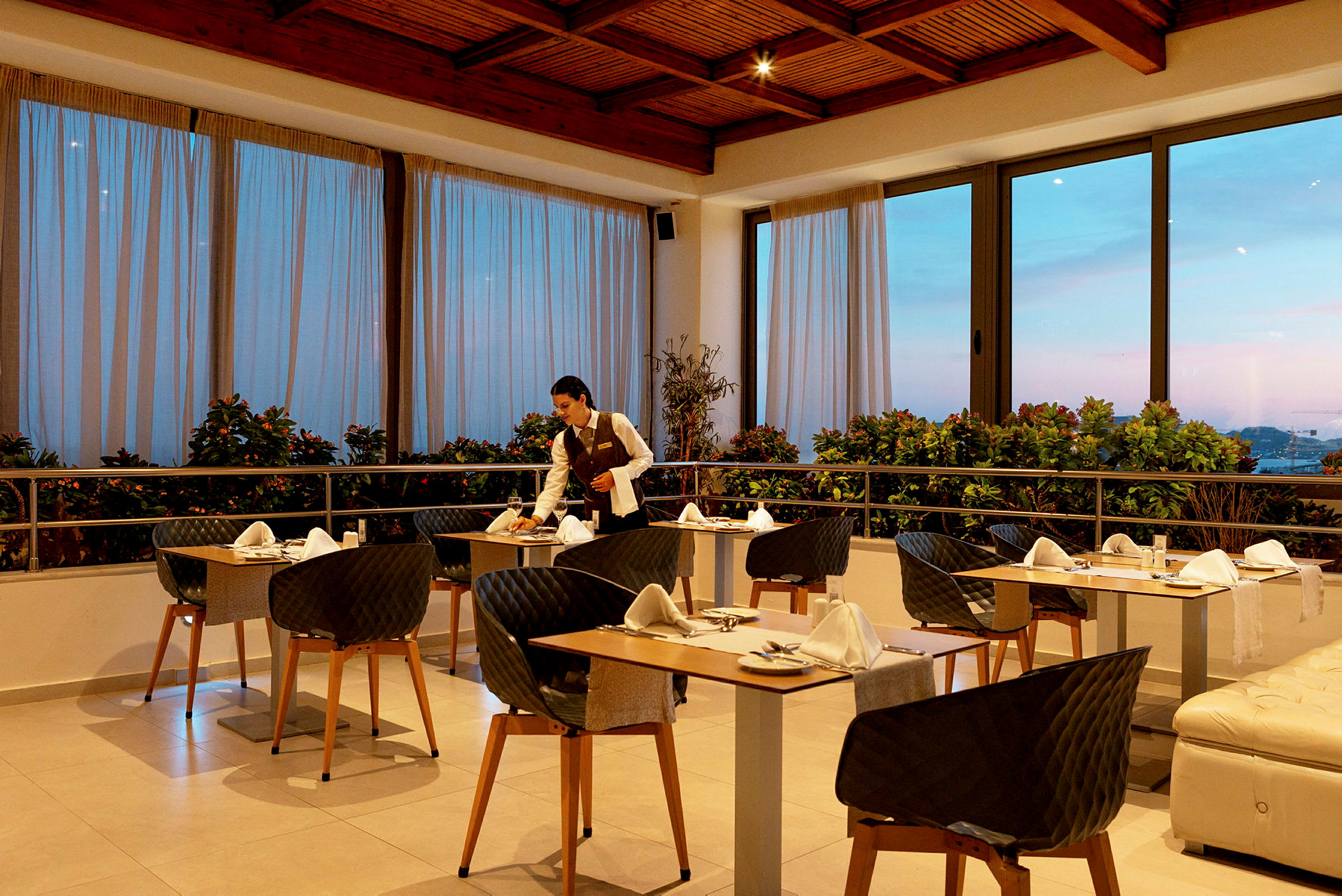 Elegant restaurant med dækkede borde og store vinduer mod altanen. (AI-genereret tekst)