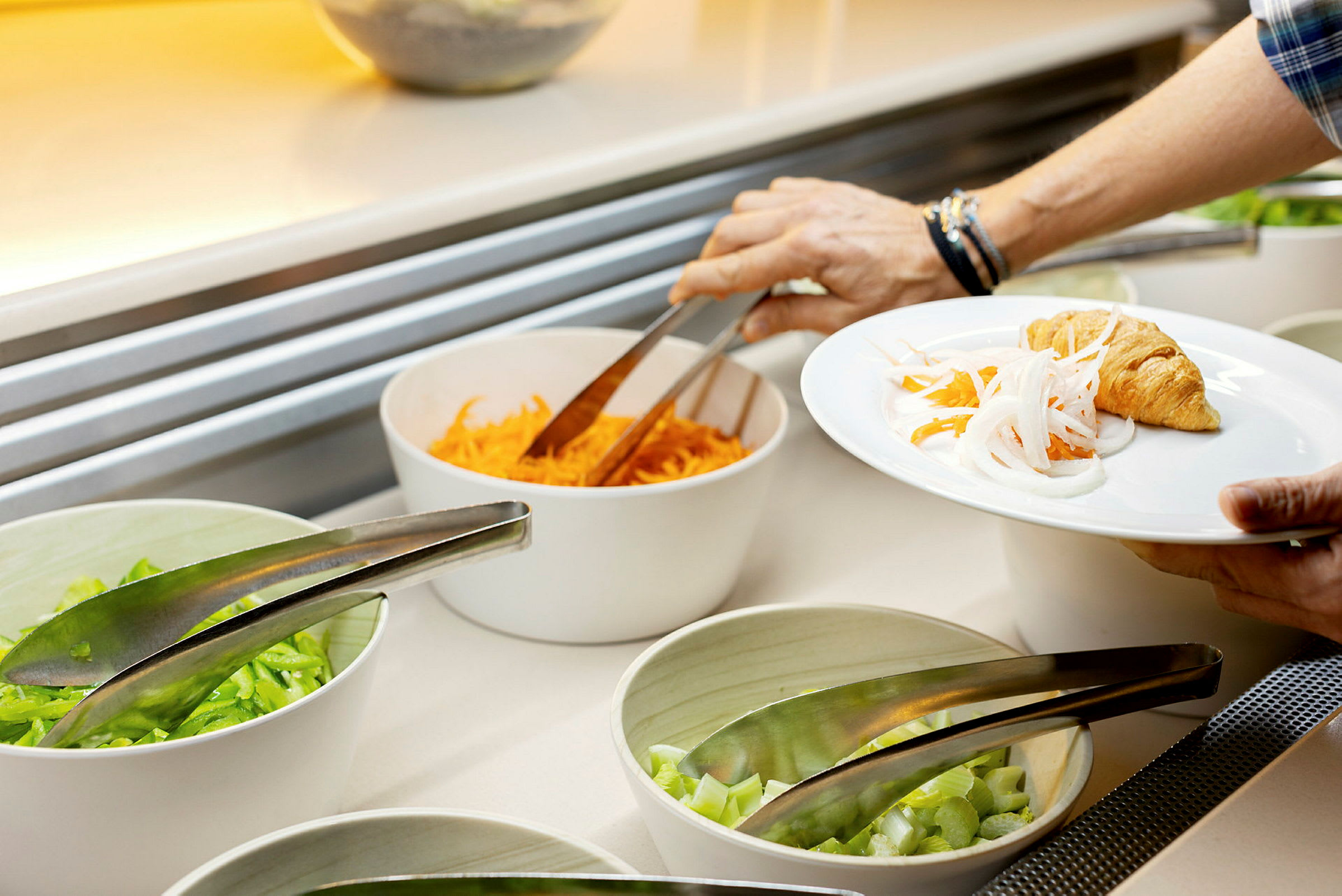 En person tager mad fra en buffet med grøntsager og bagværk. (AI-genereret tekst)