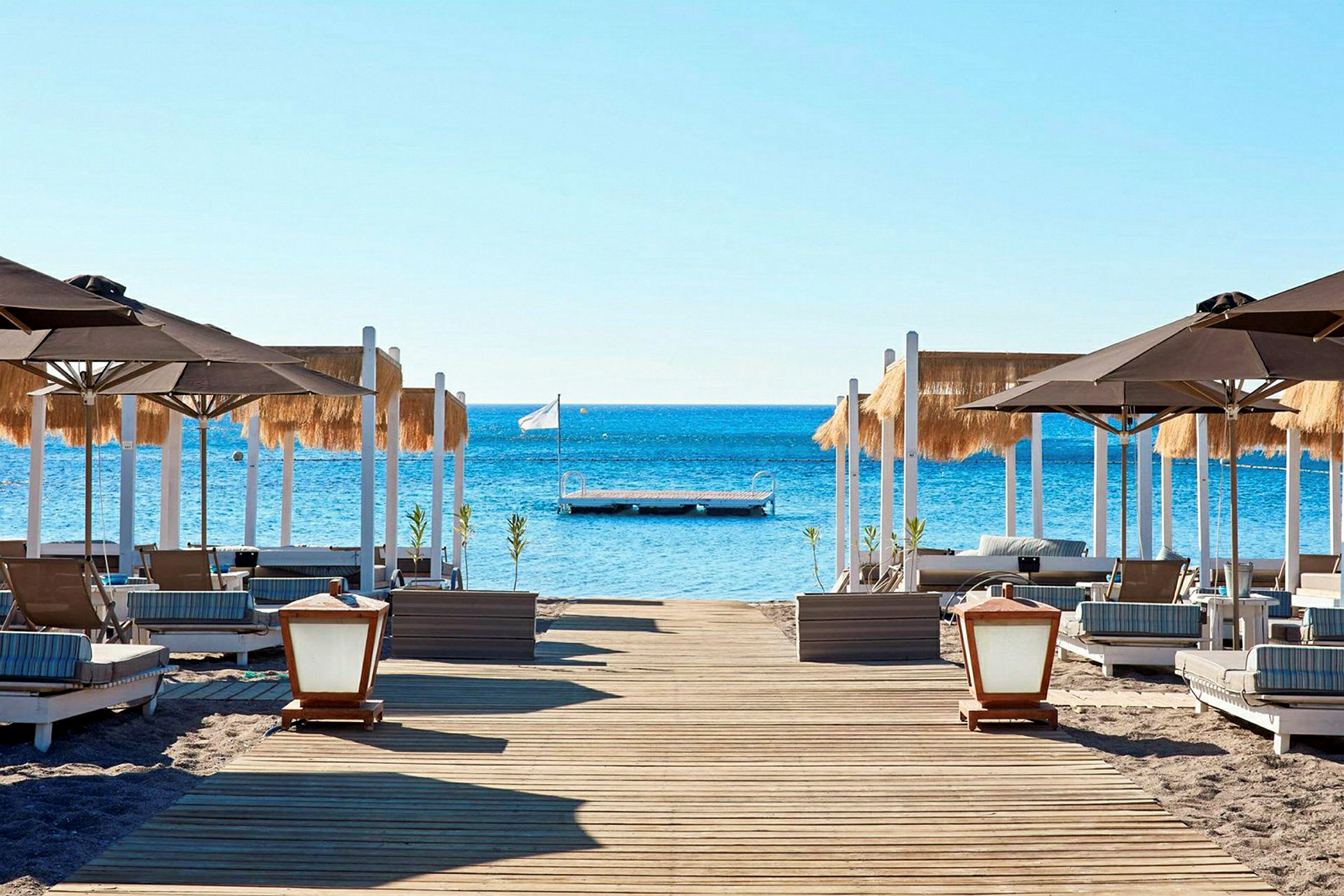 Strand med liggestole og parasoller, bro i havet. (AI-genereret tekst)