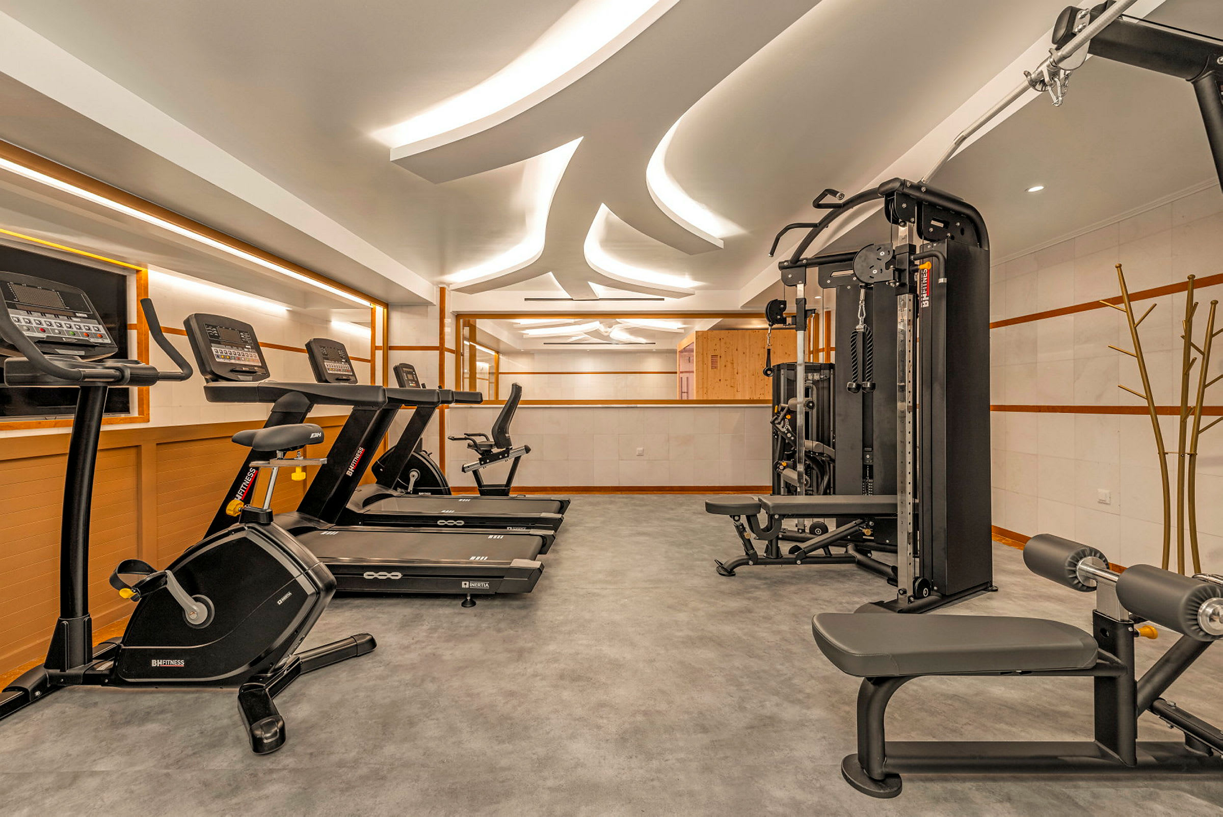 Et moderne fitnesscenter med forskellige træningsmaskiner såsom løbebånd, motionscykel og multigym. Loftbelysning og spejlvægge skaber en lys og rummelig atmosfære. (AI-genereret tekst)