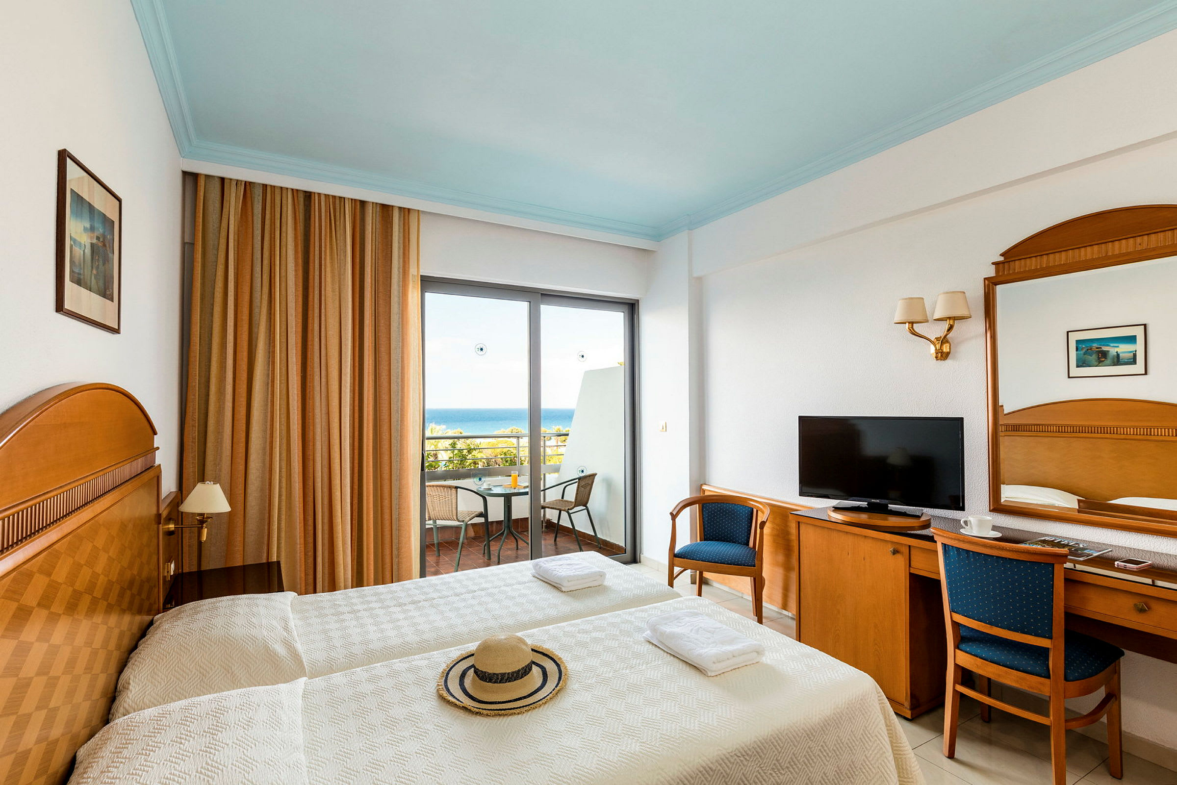 Hotelværelse med to enkeltsenge, et træskrivebord med stole og en balkon med udsigt over havet. (AI-genereret tekst)