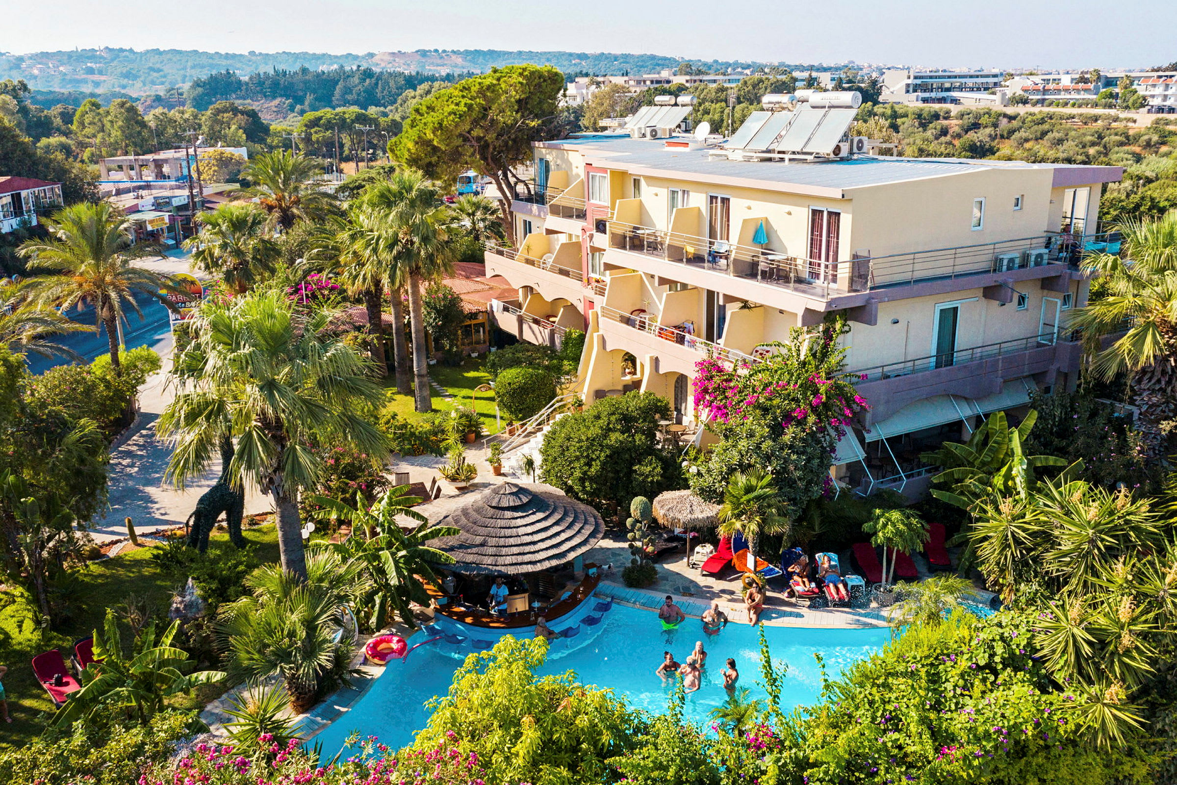 Et hotel med en udendørs pool omgivet af grønne områder og palmer. (AI-genereret tekst)