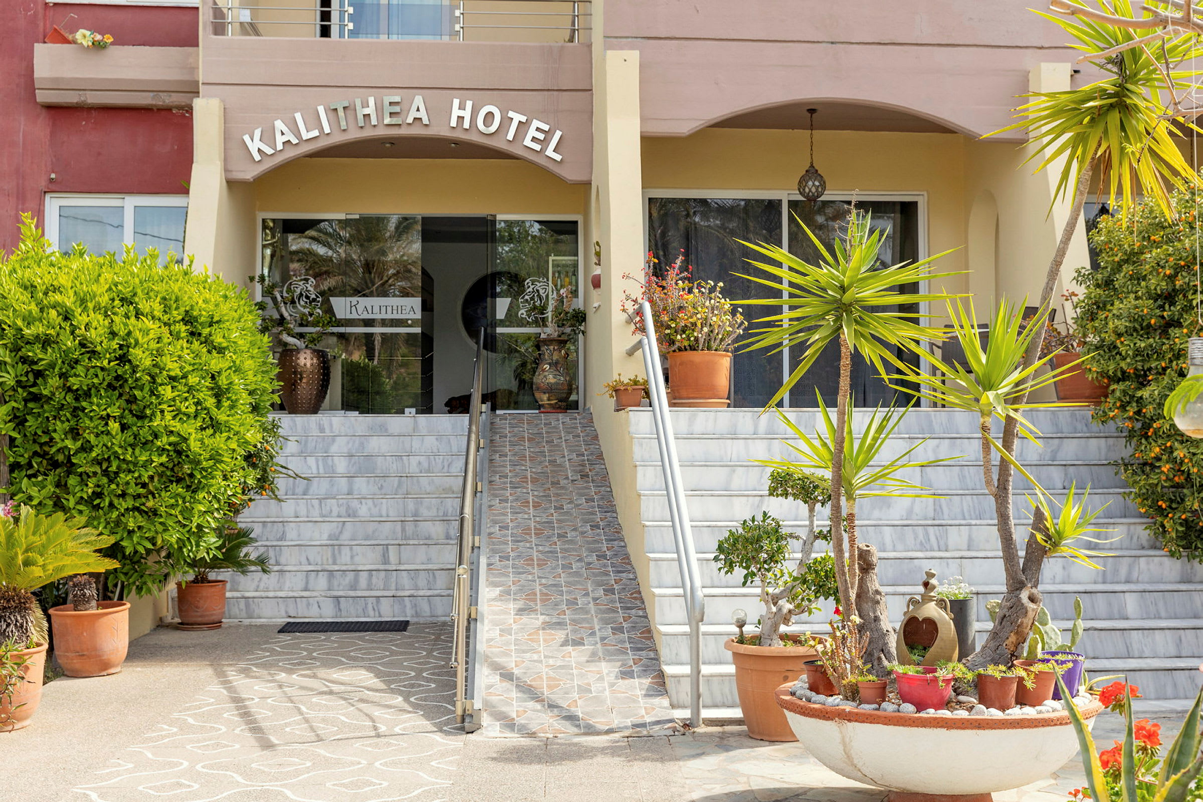 Indgangen til Kalithea Hotel med trapper og beplantning i forgrunden. (AI-genereret tekst)
