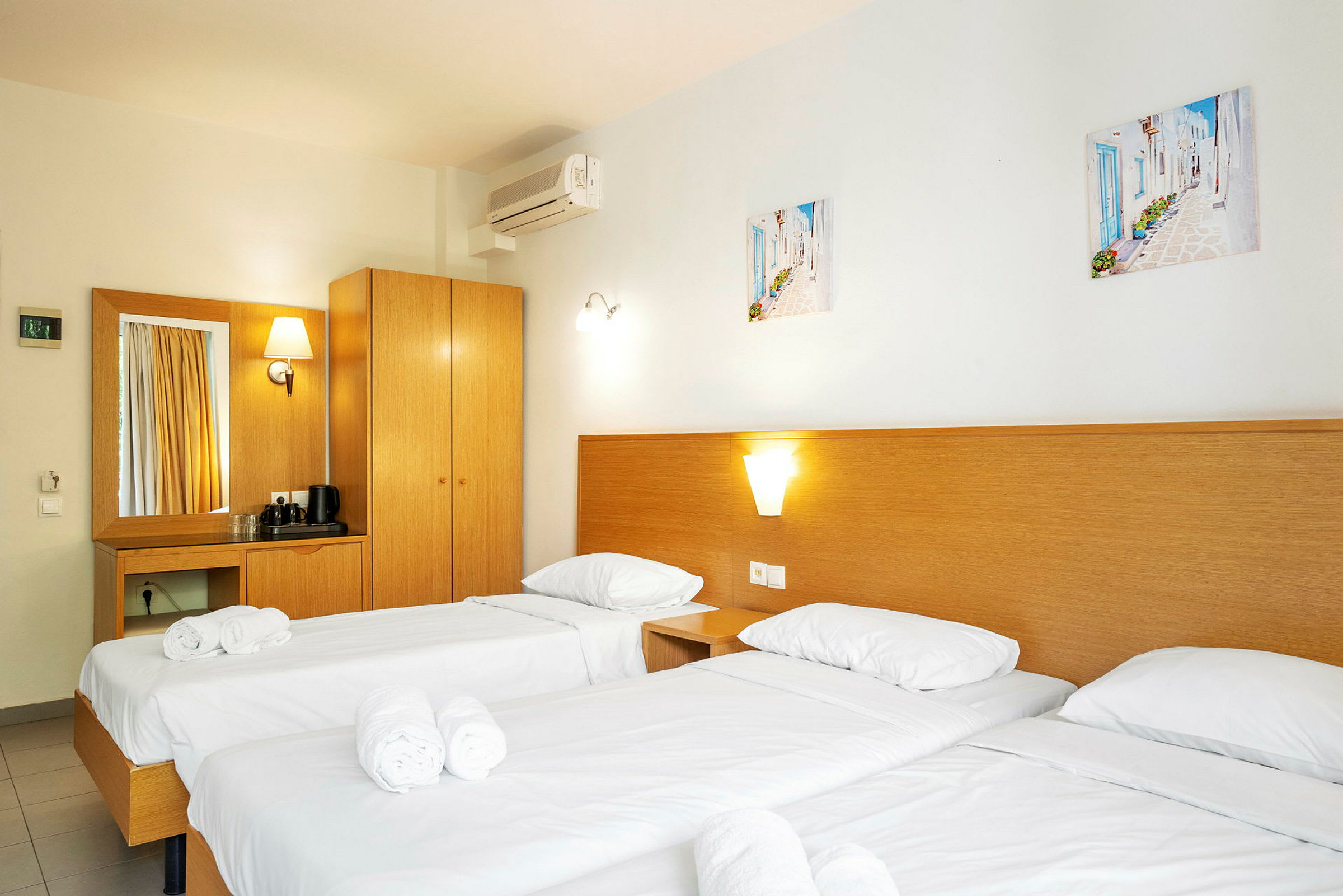 Hotelværelse med tre enkeltsenge, indrettet med hvidt sengetøj og rullede håndklæder. (AI-genereret tekst)
