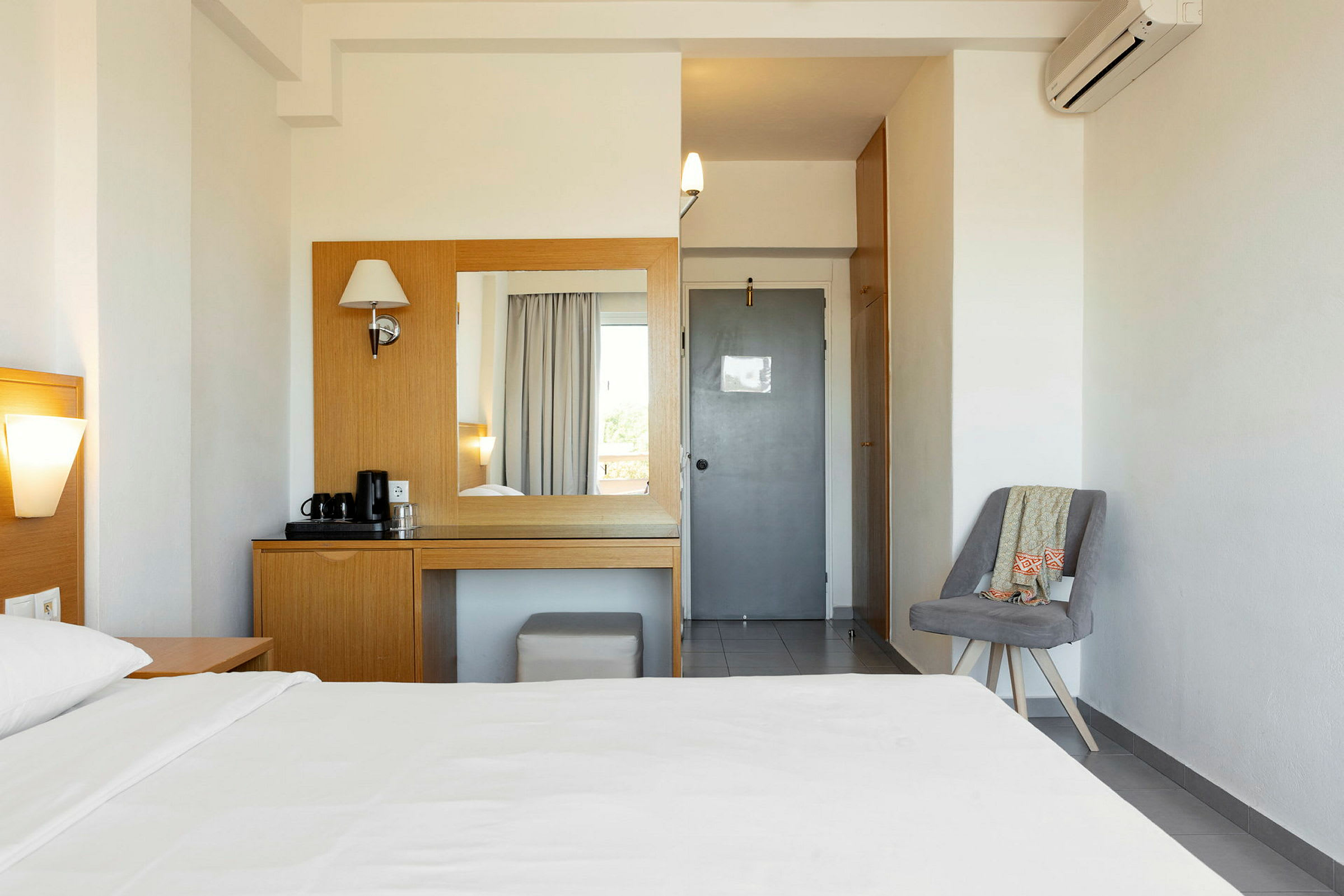Et hotelværelse med en seng, et bord og spejl til toiletartikler samt en stol ved siden af. (AI-genereret tekst)