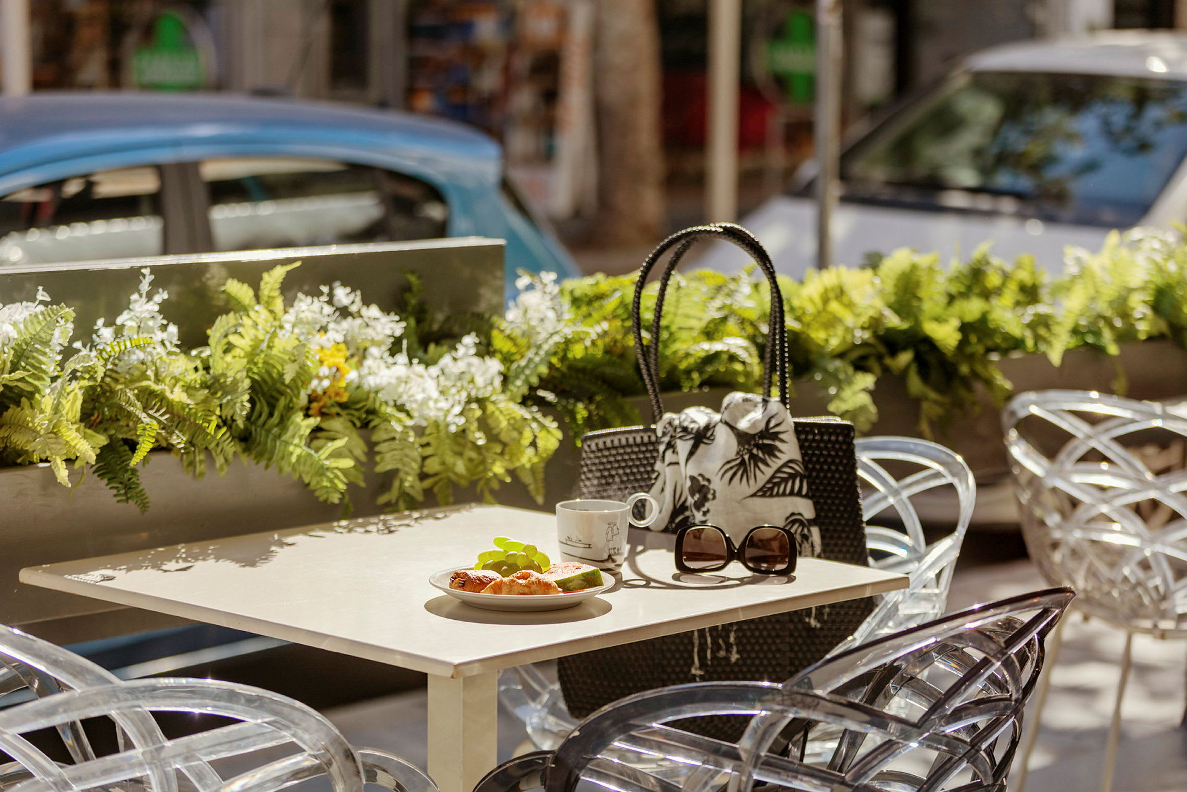 Bord med croissant, kop og solbriller på udendørs café med blomsterdekorationer. (AI-genereret tekst)