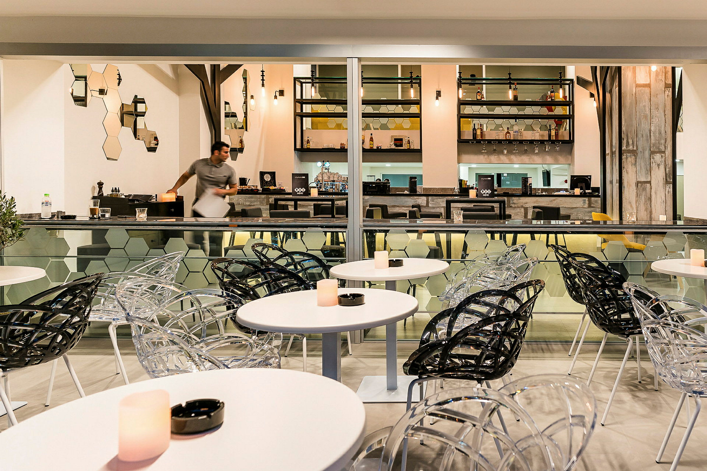 En moderne café med gennemsigtige og sorte stole samt hvide borde. Bagved er der en velbelyst bar. (AI-genereret tekst)