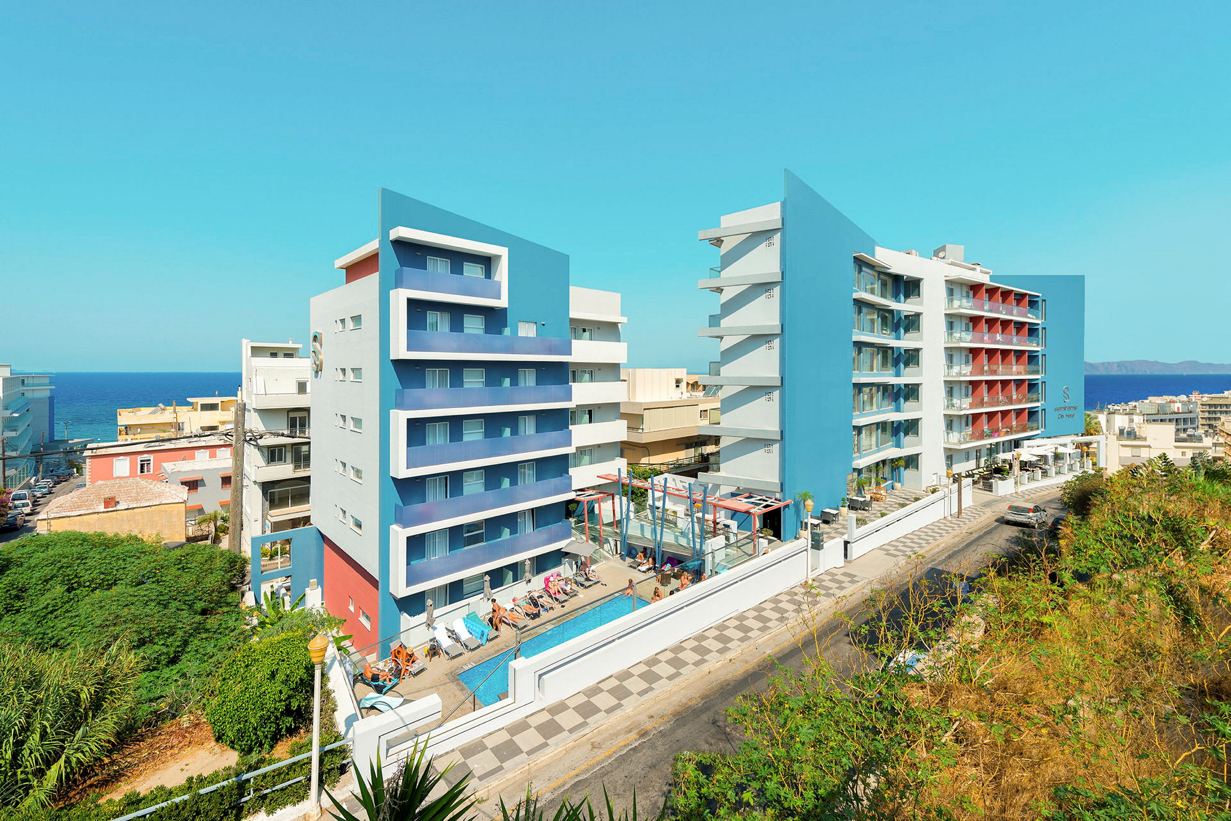 Billede af to moderne hotelbygninger med blå facader, en swimmingpool og liggestole i forgrunden. (AI-genereret tekst)