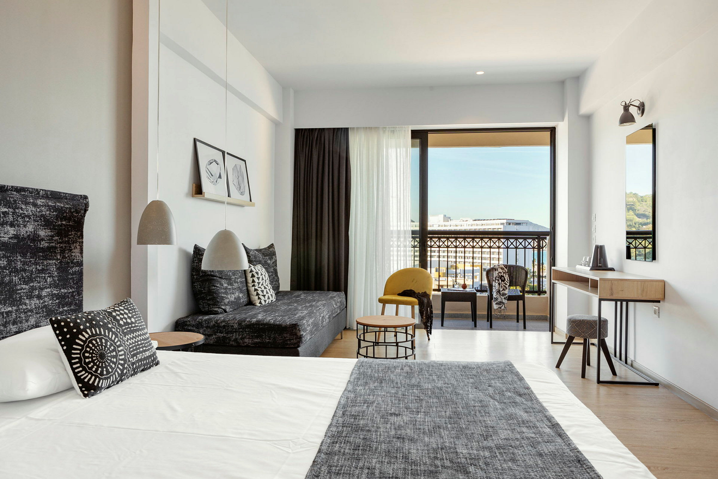 Moderne hotelværelse med seng, sofa og siddegruppe samt udsigt til balkon og omgivelser. (AI-genereret tekst)