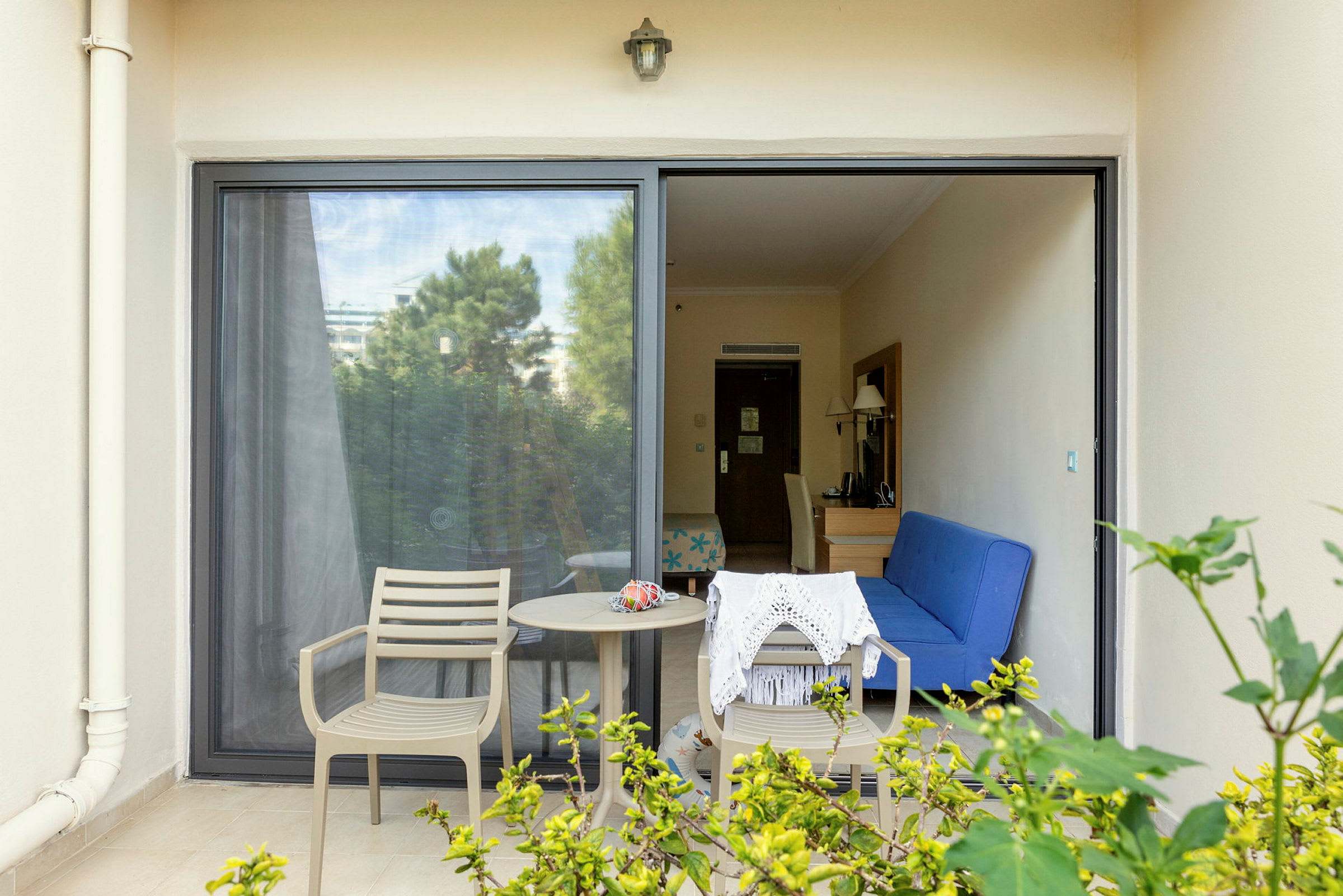 Billede af en terrasse med to stole, et bord og udsigt ind i et hotelværelse. (AI-genereret tekst)