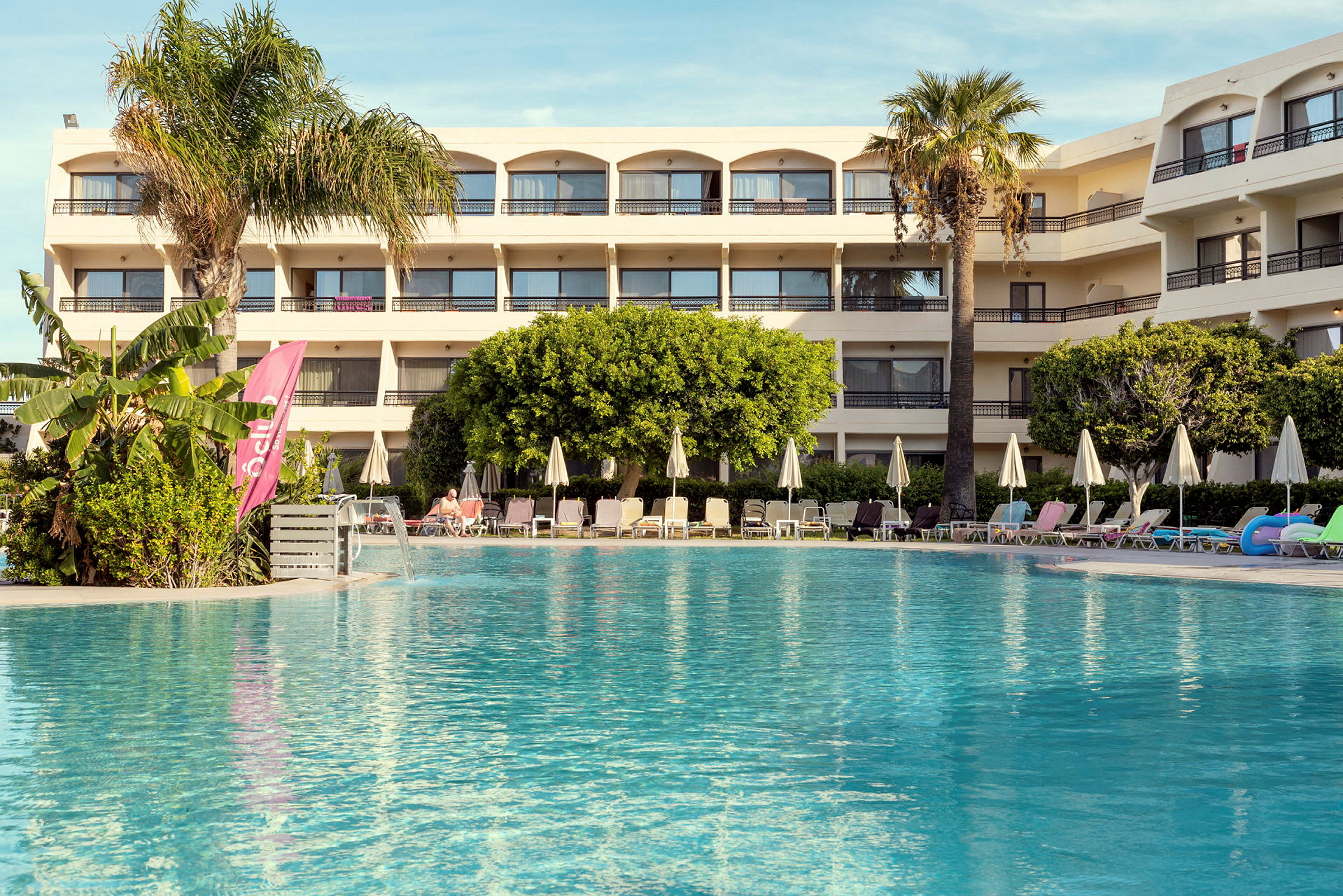 Hotel med pool og liggestole i forgrunden. (AI-genereret tekst)