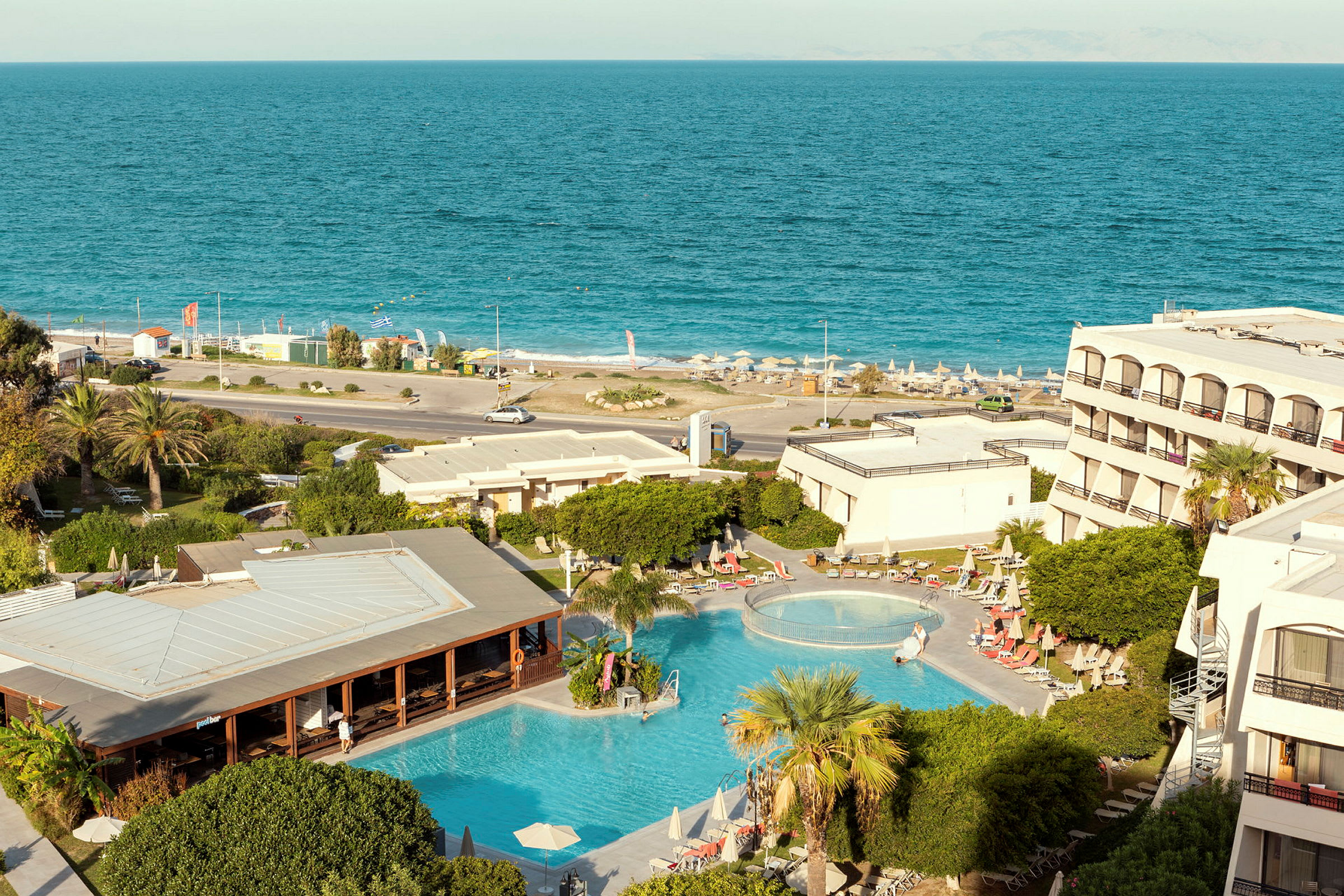 Billede af hotelområde med pool, grønt område og udsigt til havet. (AI-genereret tekst)