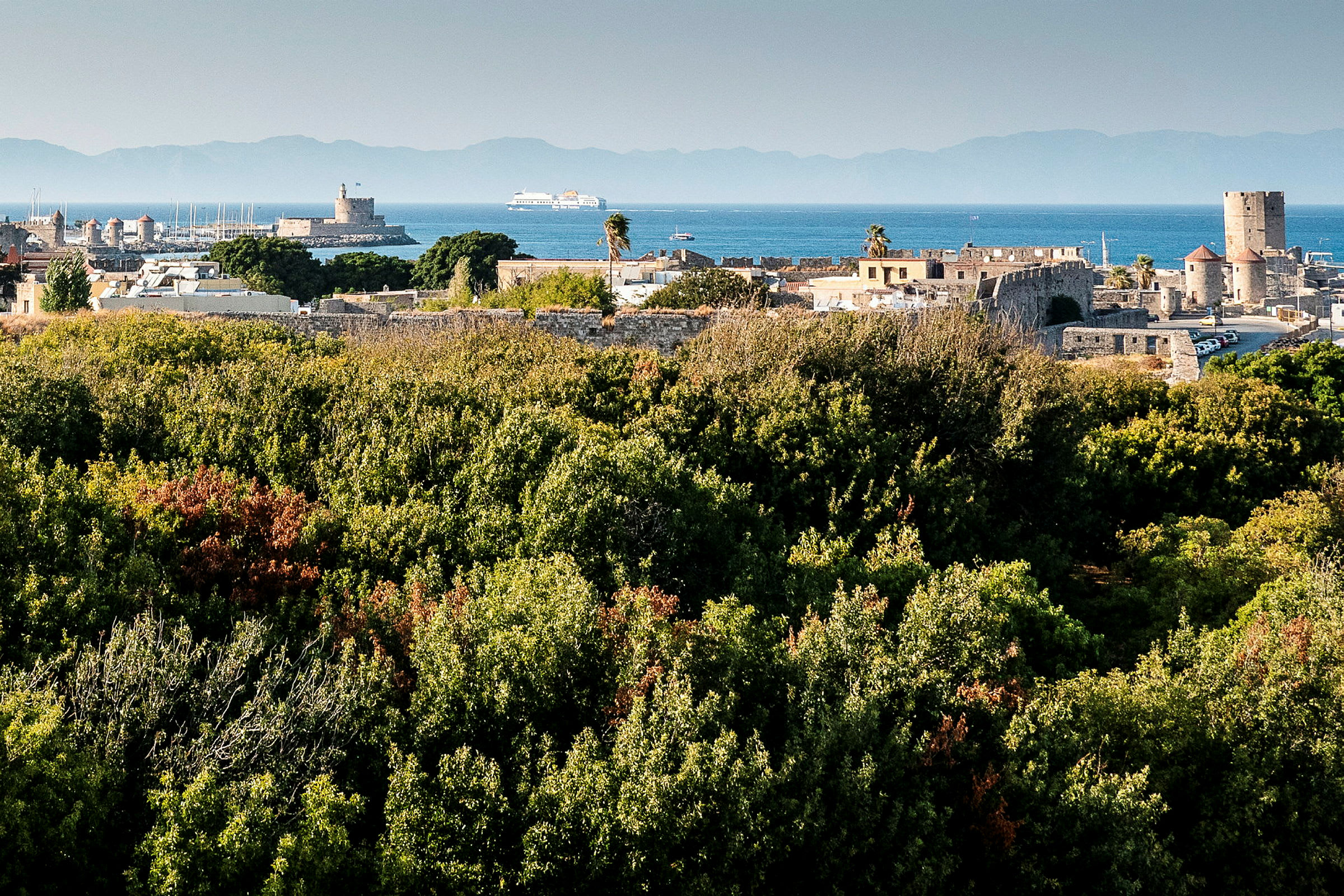Udsigt over grønne områder og historiske bygninger ved havet. (AI-genereret tekst)