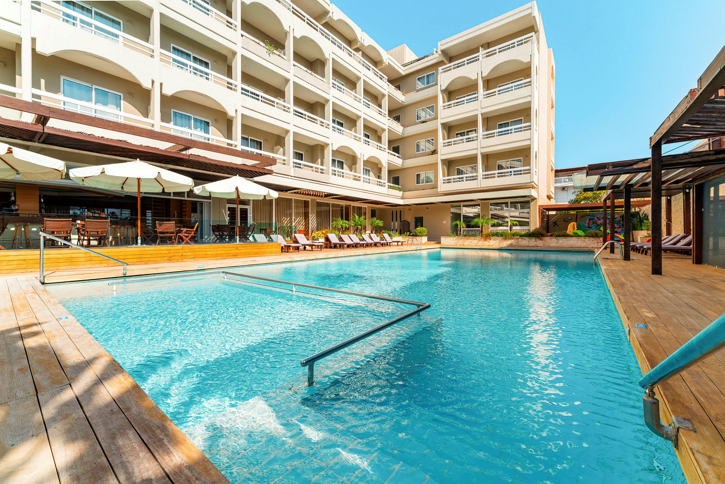 Udendørs pool med liggestole og parasoller ved et fleretagers hotel. (AI-genereret tekst)