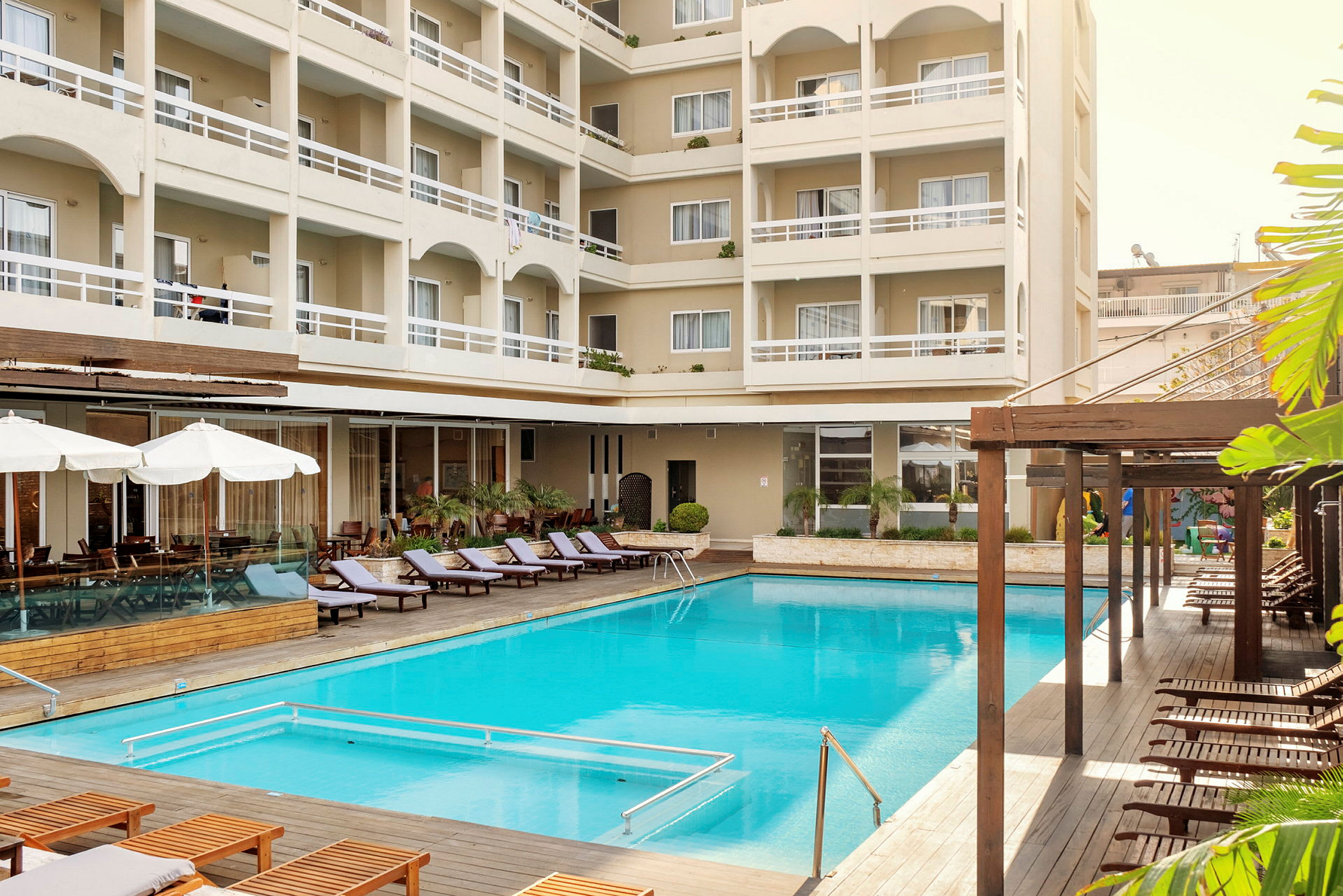 Hotelbygning med altaner og liggestole ved en udendørs pool. (AI-genereret tekst)