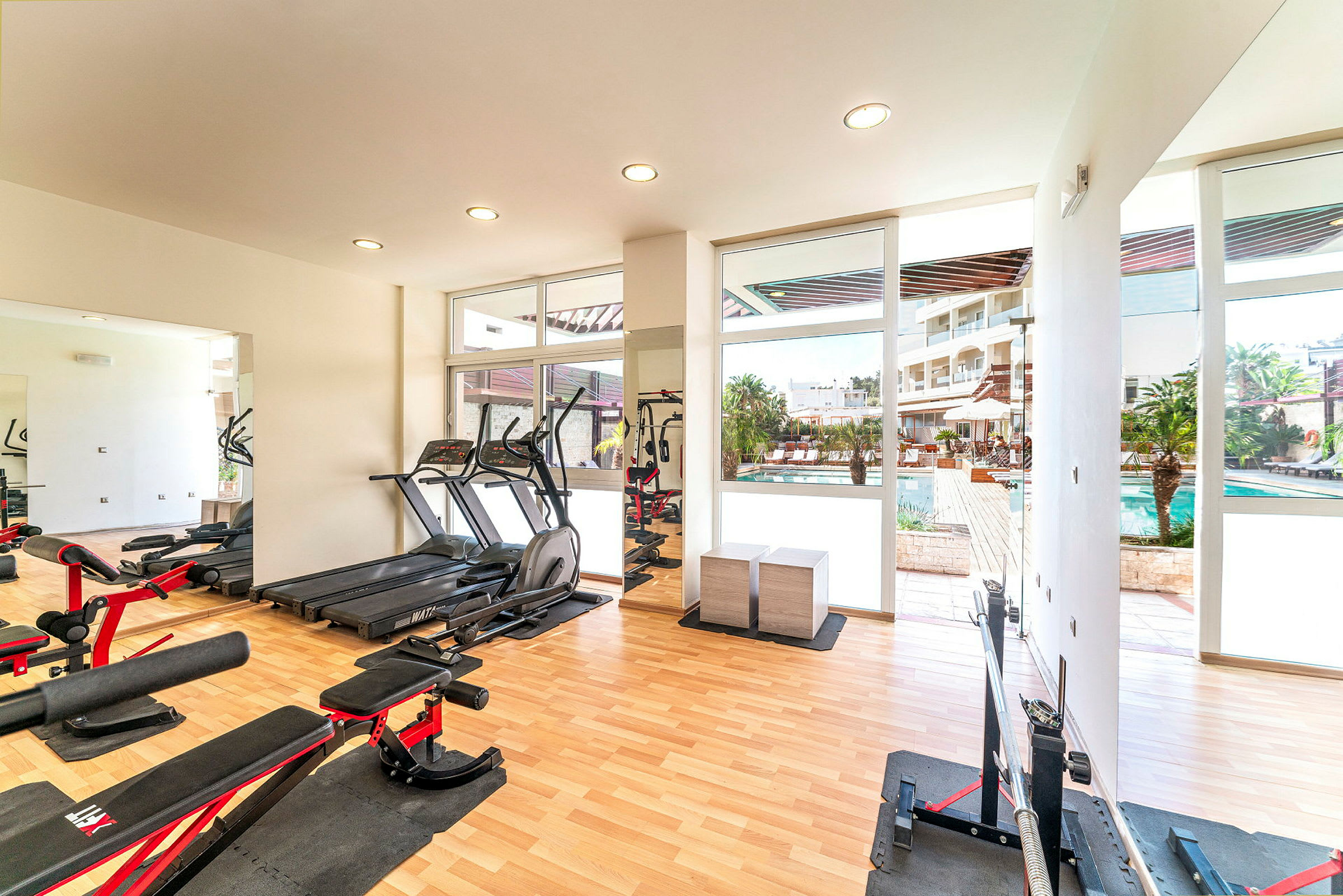Et fitnesscenter med træningsudstyr og vinduer, der viser en udendørs swimmingpool. (AI-genereret tekst)