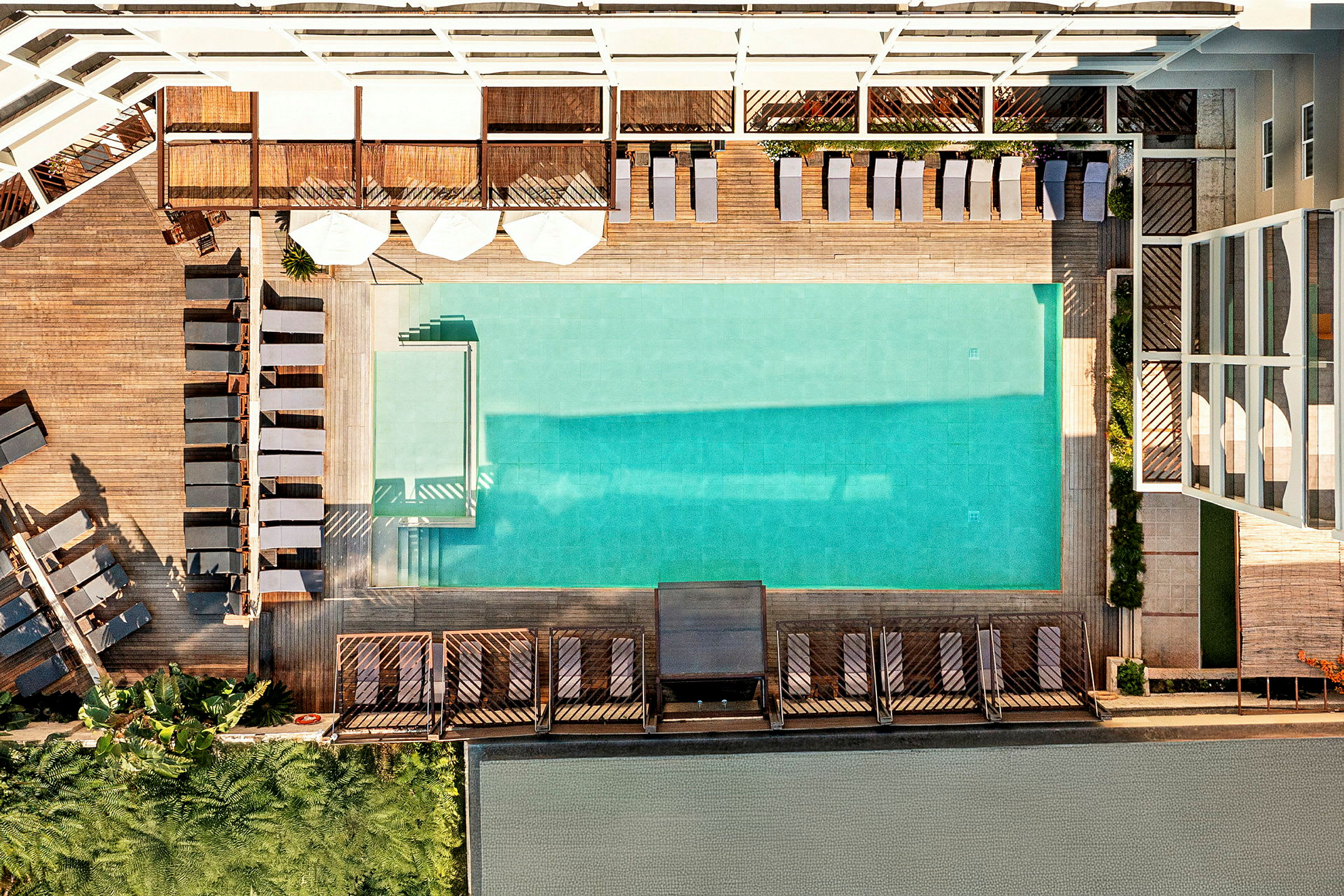 Billedet viser en udendørs pool omgivet af liggestole og trædæk. (AI-genereret tekst)