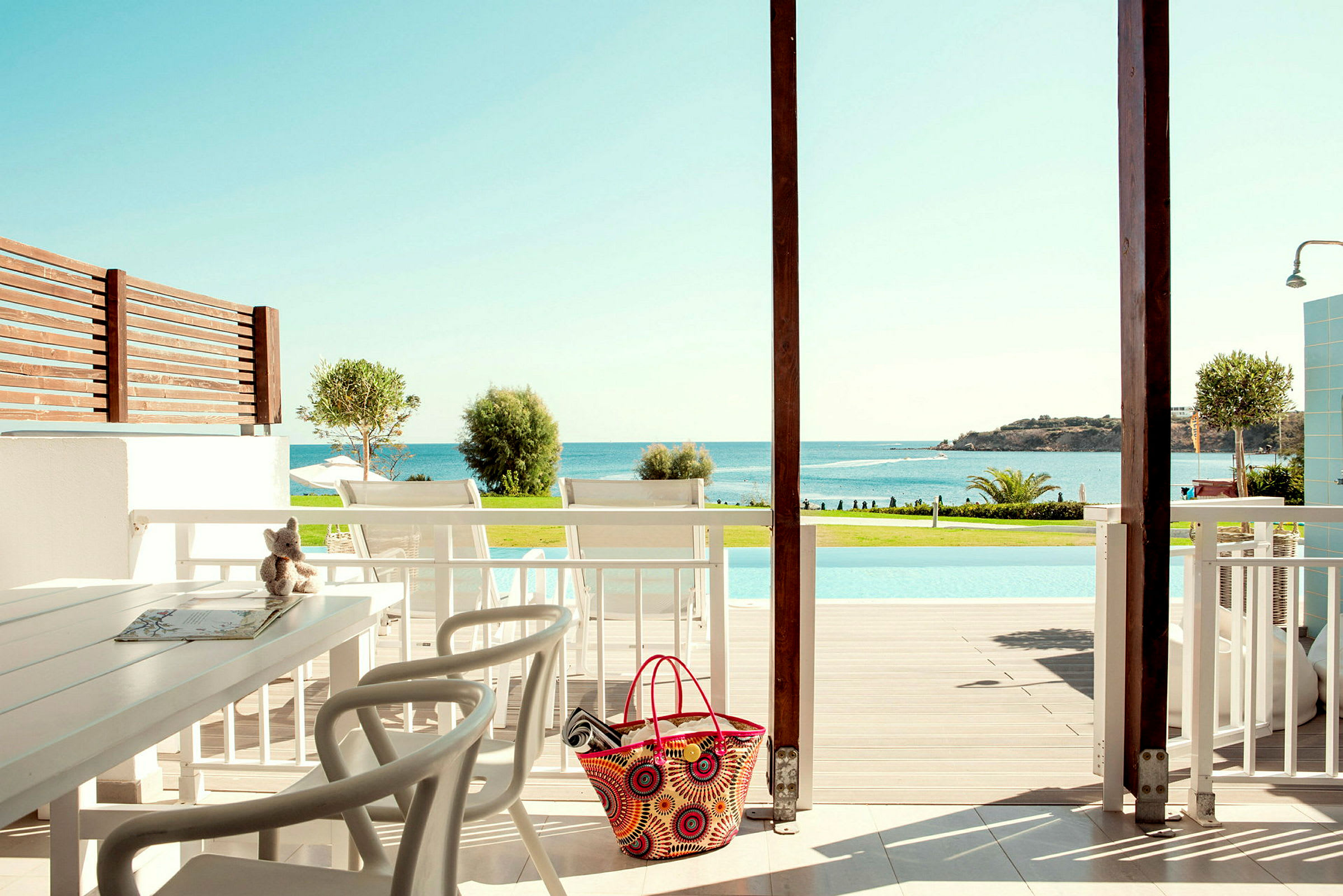 Udsigt fra en terrasse med siddeområde mod en pool og havet. (AI-genereret tekst)
