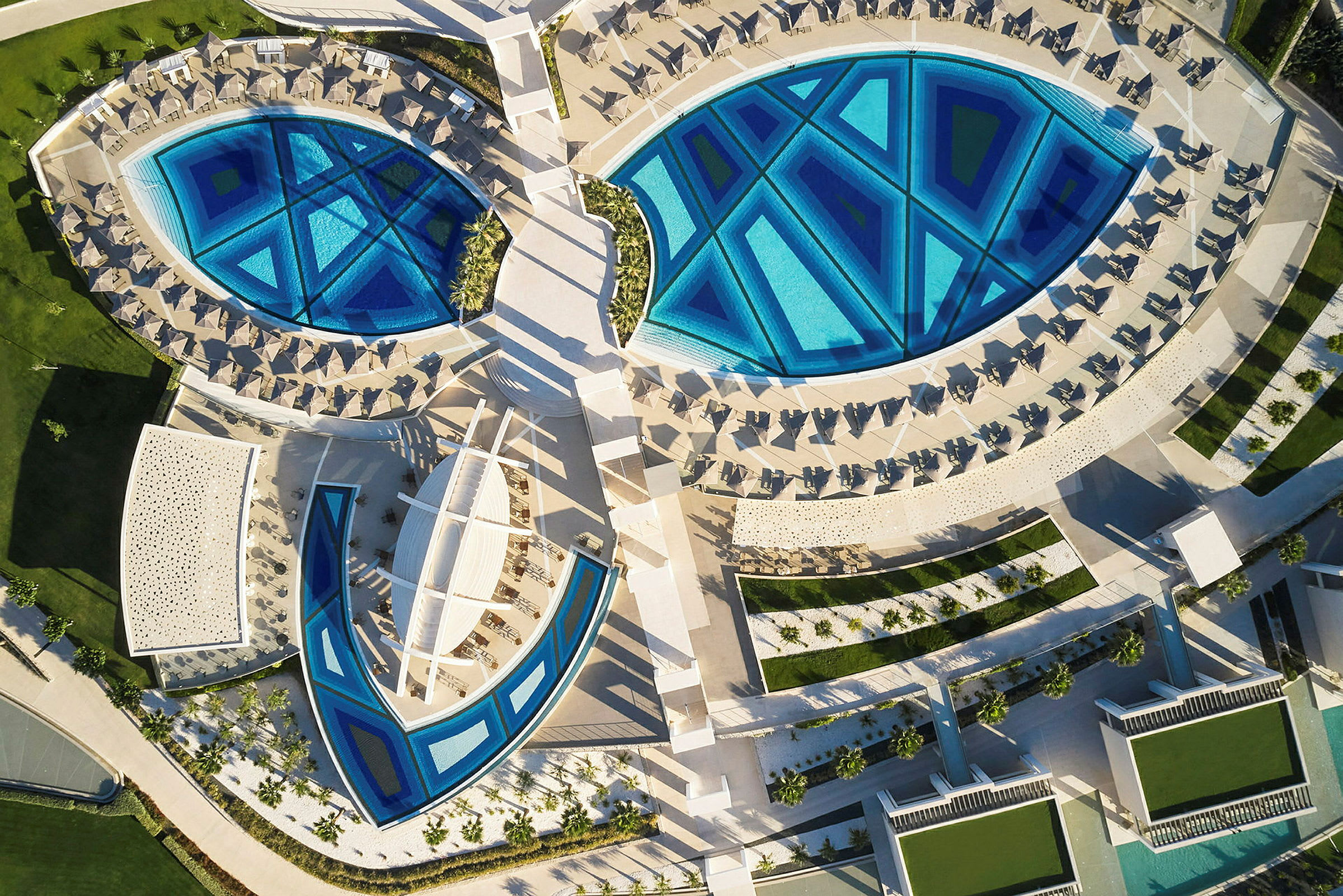 Luftfoto af en resort med geometriske swimmingpools og liggestole. (AI-genereret tekst)