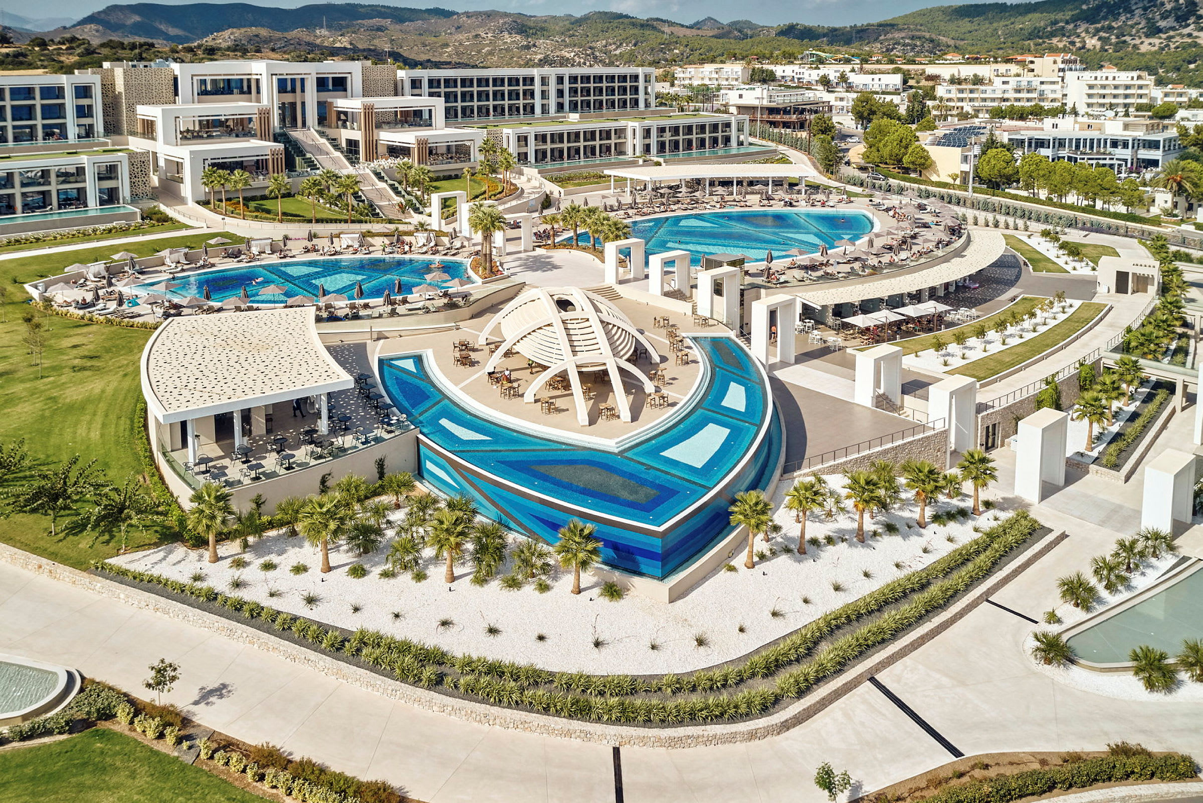 Hotelkompleks med swimmingpools og moderne bygninger i et grønt omkringliggende landskab. (AI-genereret tekst)