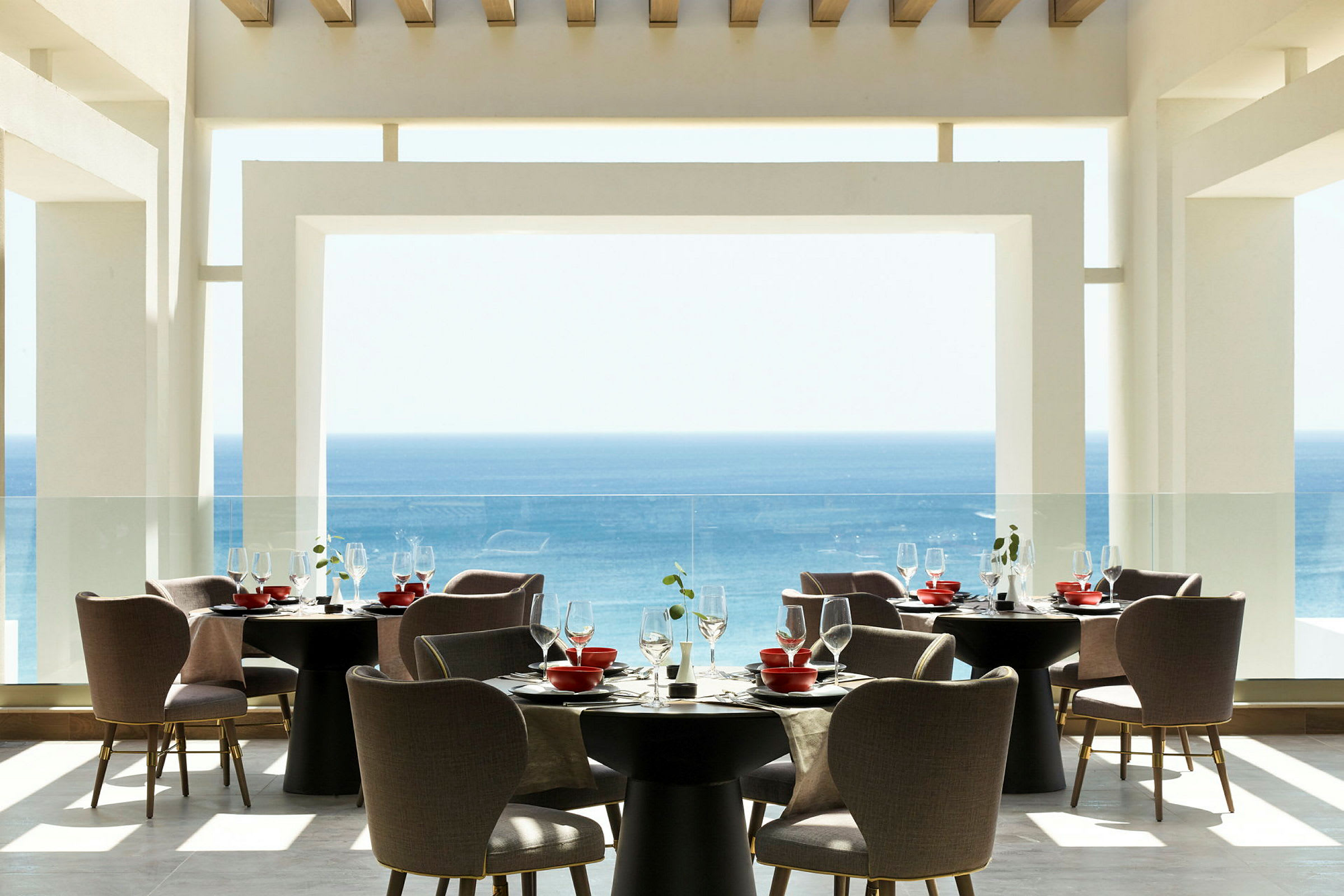 En moderne restaurant med udsigt over havet, møbleret med runde borde og behagelige stole. (AI-genereret tekst)