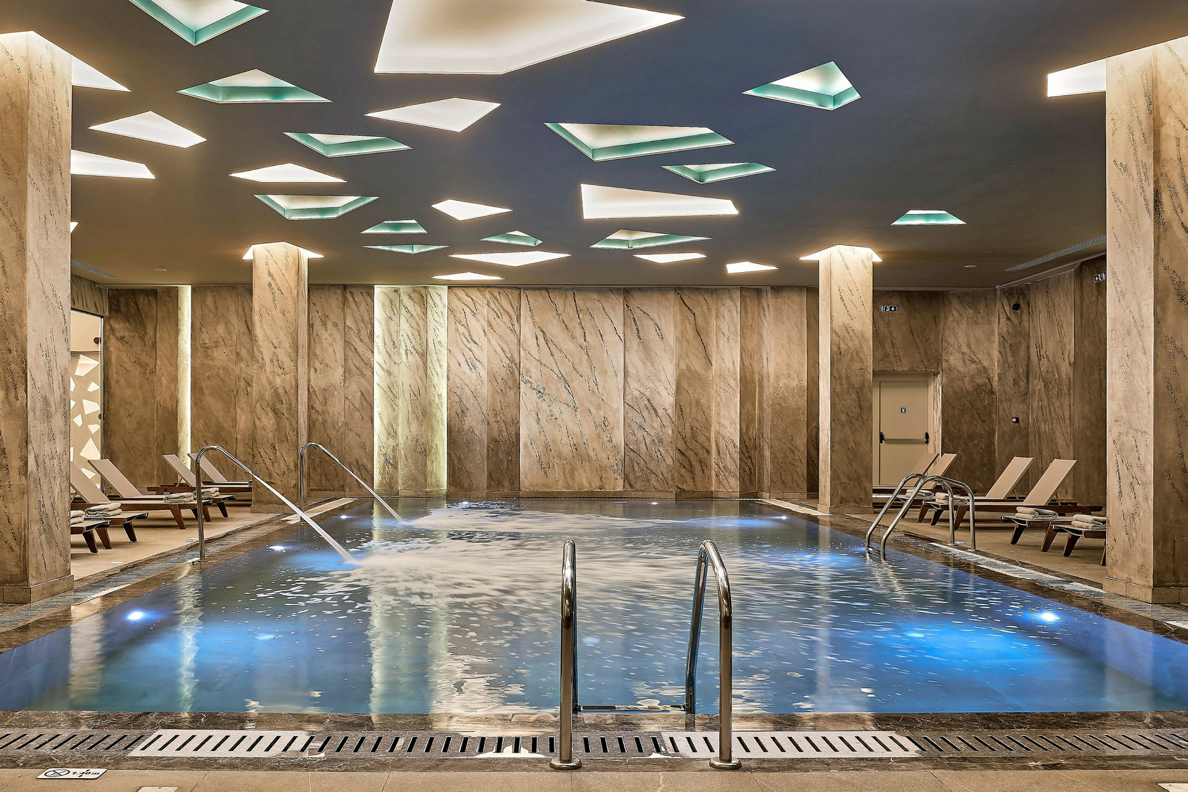 Indendørs pool med marmormønstrede vægge og loft med geometriske lyselementer. (AI-genereret tekst)