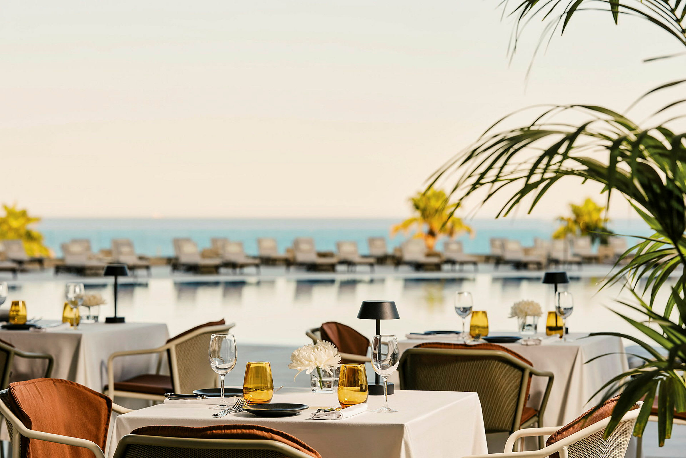 En restaurant med opdækkede borde ved en pool med liggestole og udsigt over havet. (AI-genereret tekst)